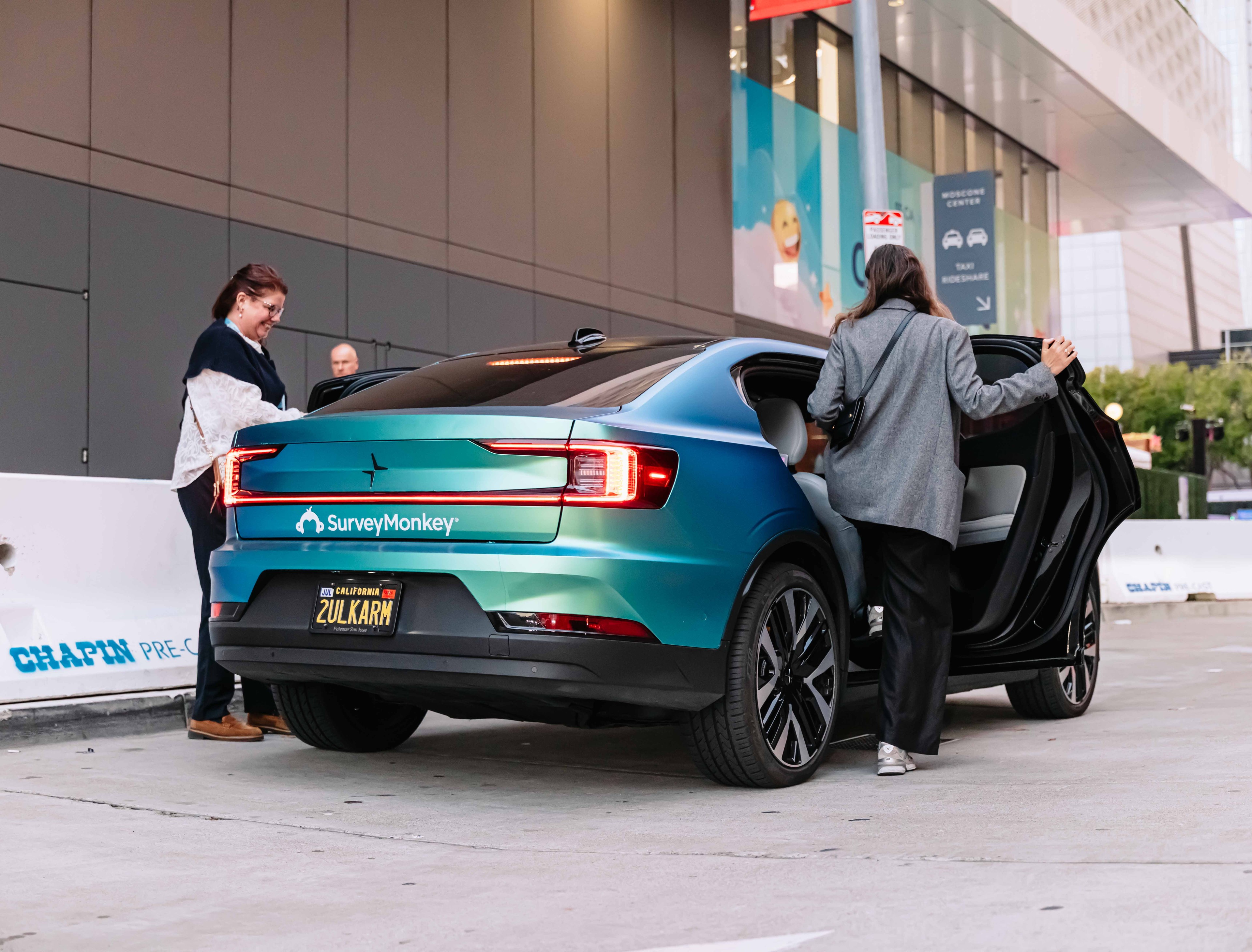 Passengers boarding a SurveyMonkey-branded teal Polestar