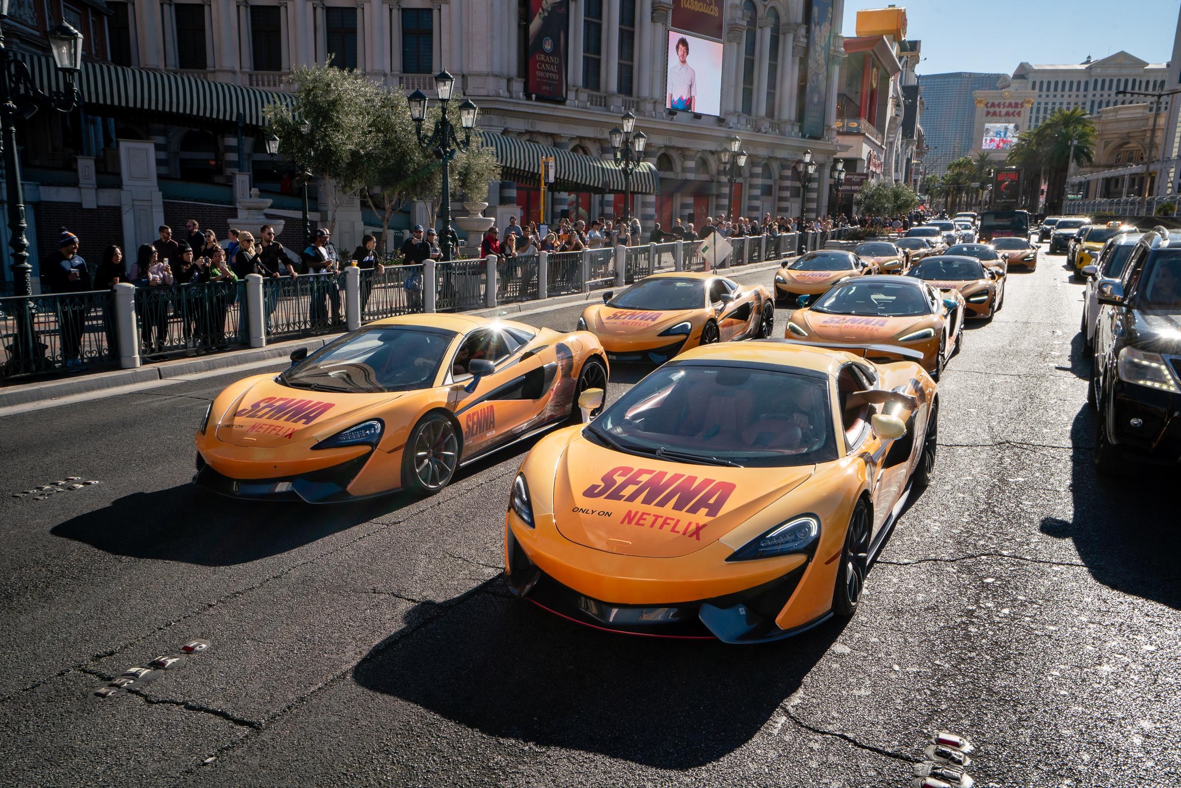 Fleet of Netflix Senna-branded orange McLaren supercars parading down the Las Vegas Strip in front of crowds of spectators