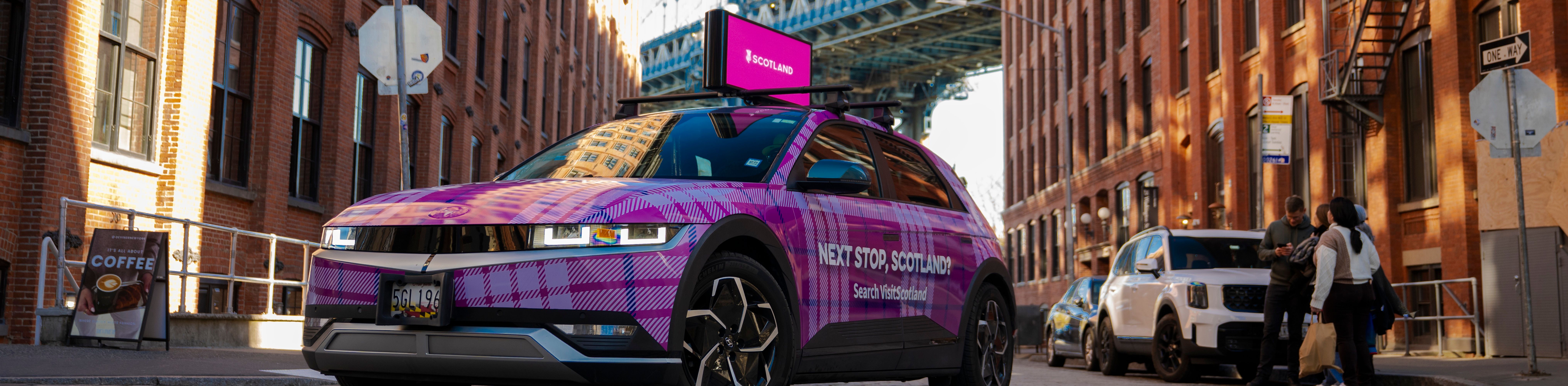 Tartan-wrapped car with "Next Stop Scotland?" written on it and a digital top that reads SCOTLAND