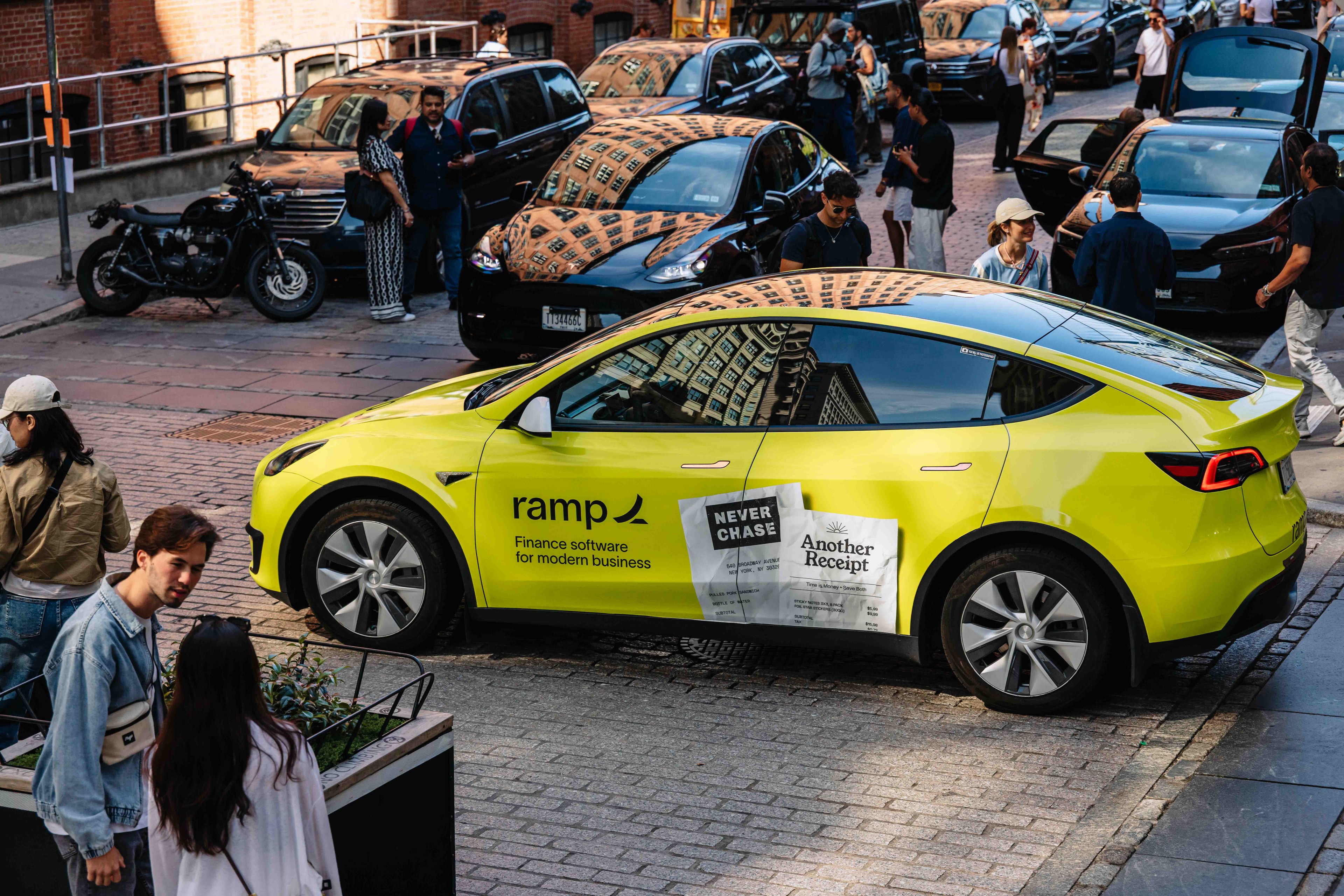 Ramp Finance neon yellow-wrapped Tesla Model Y parked on a cobblestone New York City street surrounded by pedestrians
