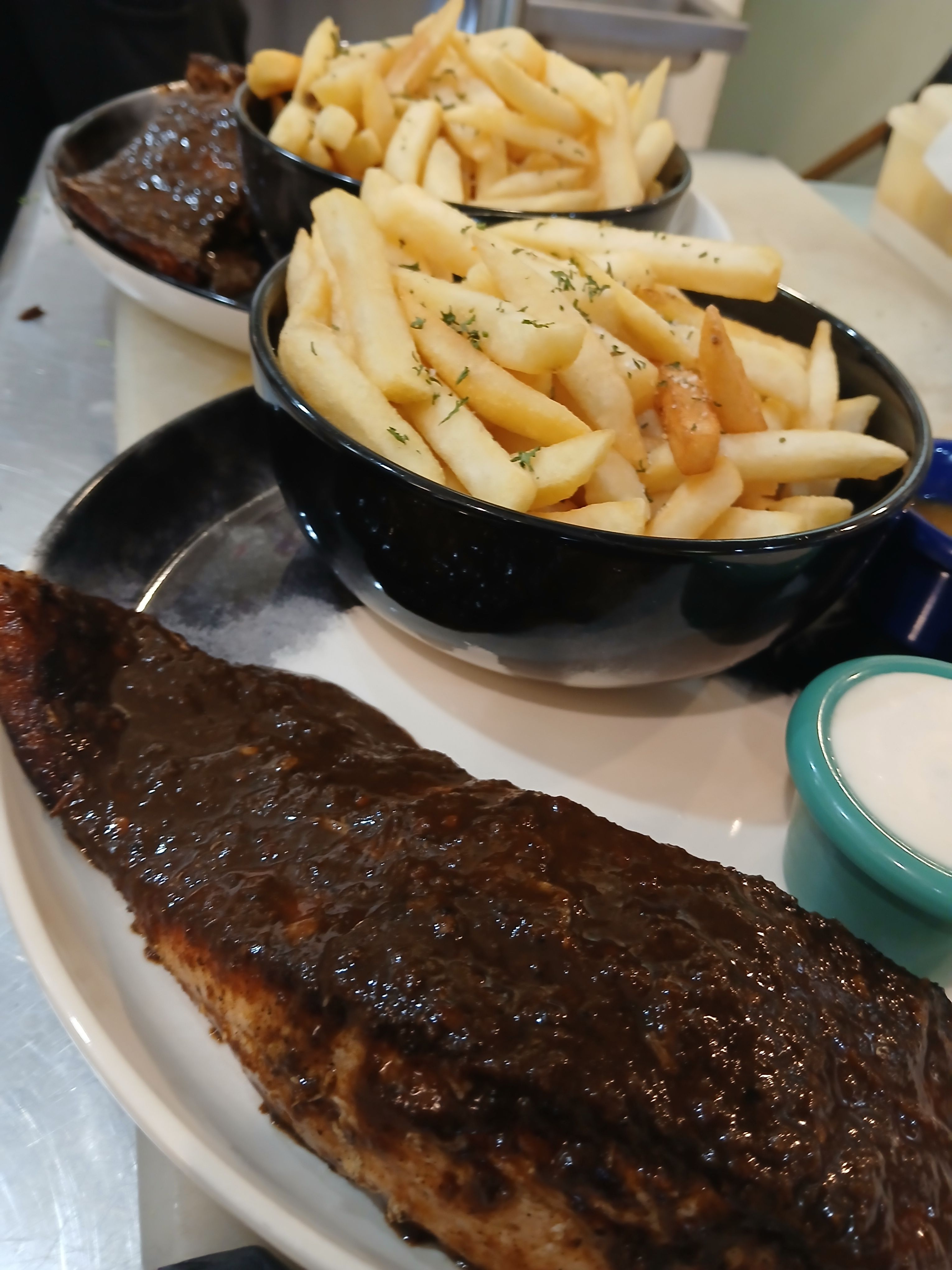A signature seared jerk salmon fillet served with a bowl of crispy golden fries and dipping sauces at Jus Fishy & Beyond.