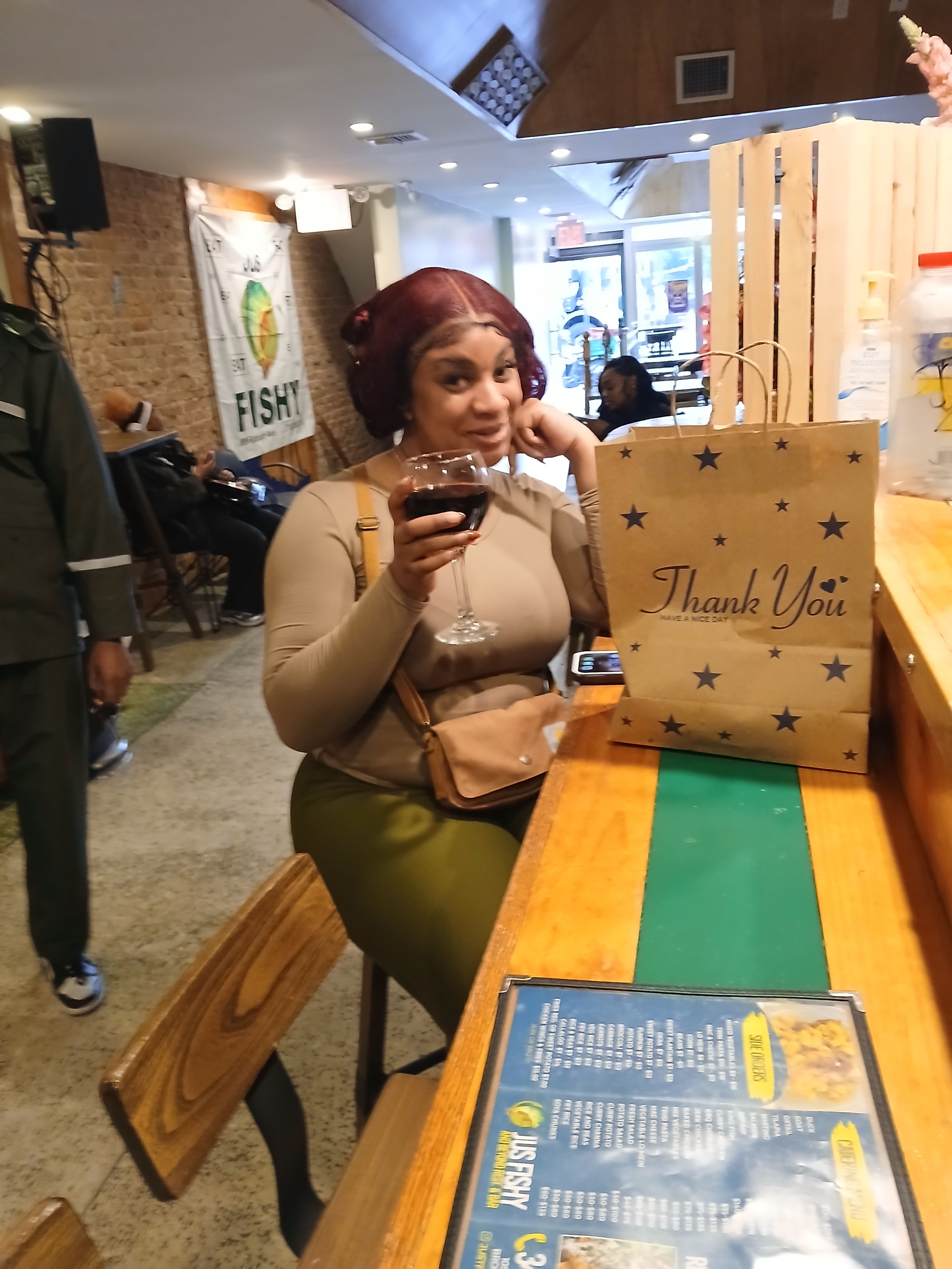  A happy customer enjoying a glass of wine at the Jus Fishy & Beyond bar, featuring our Caribbean seafood takeout bag and full menu on Flatbush Ave.