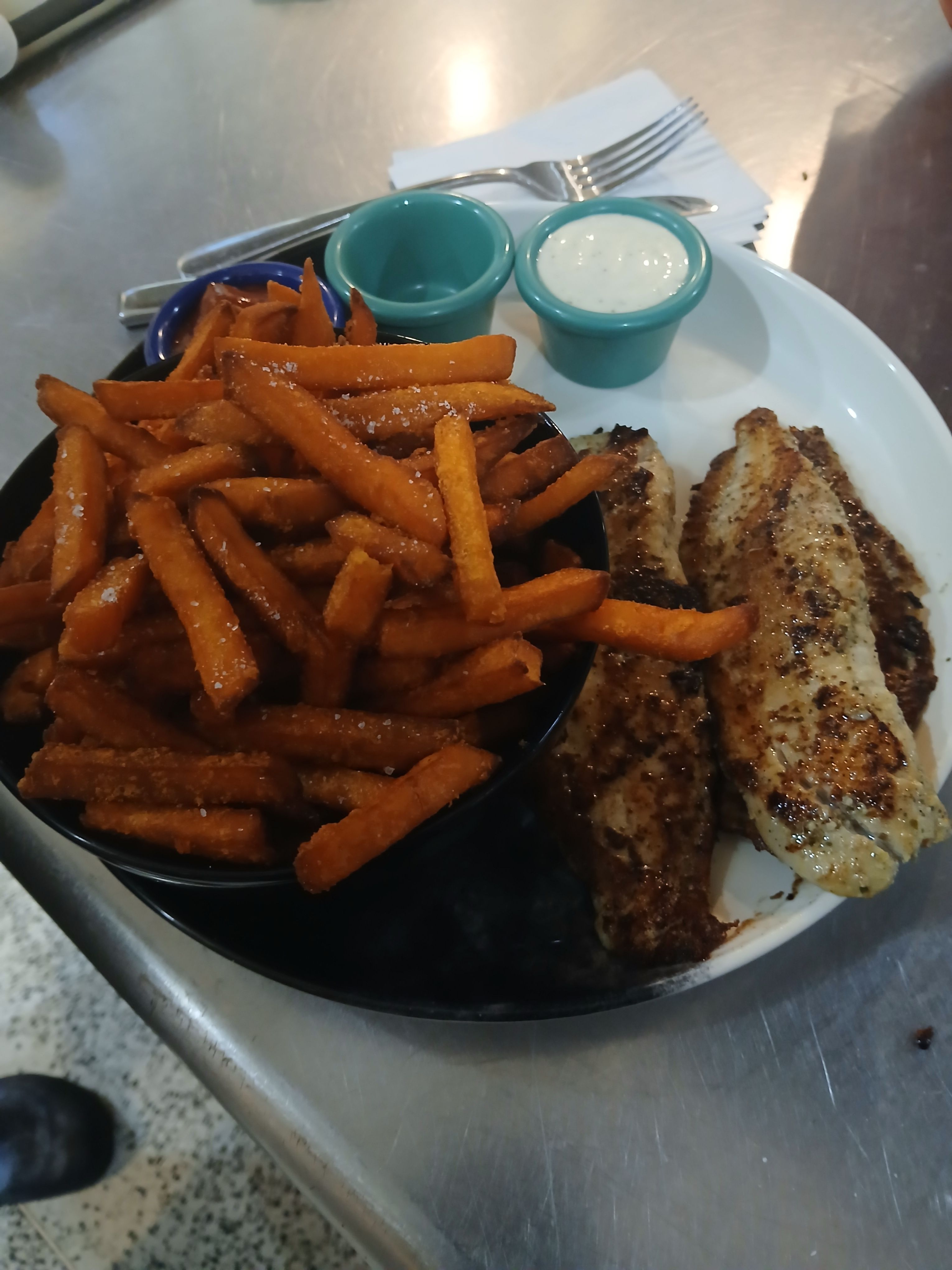 A fresh grilled fish fillet served with a large portion of crispy sweet potato fries and signature house dipping sauces.