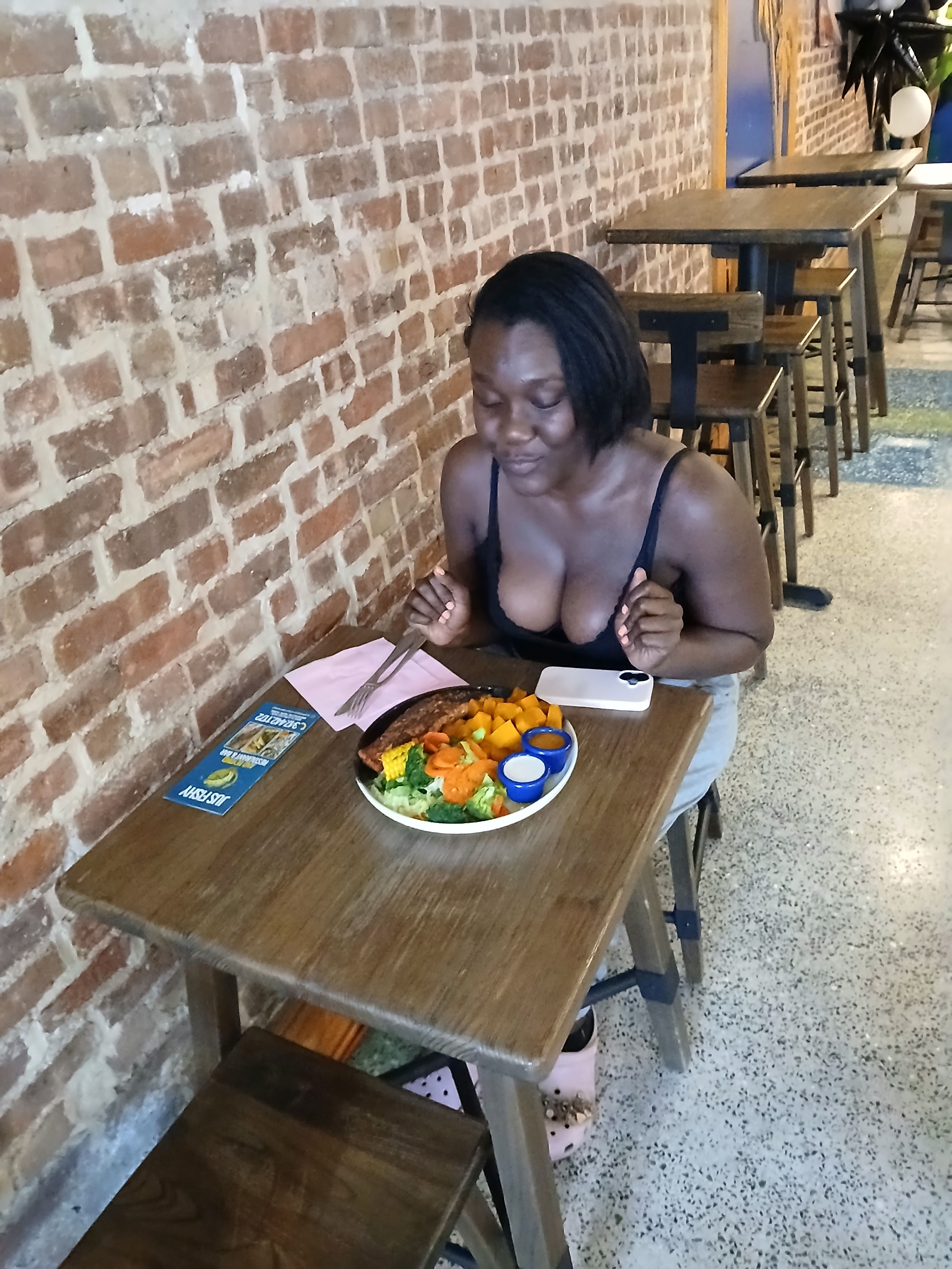 A customer smiling and enjoying a healthy grilled seafood platter in the rustic, brick-walled dining room of our Flatbush Avenue restaurant.