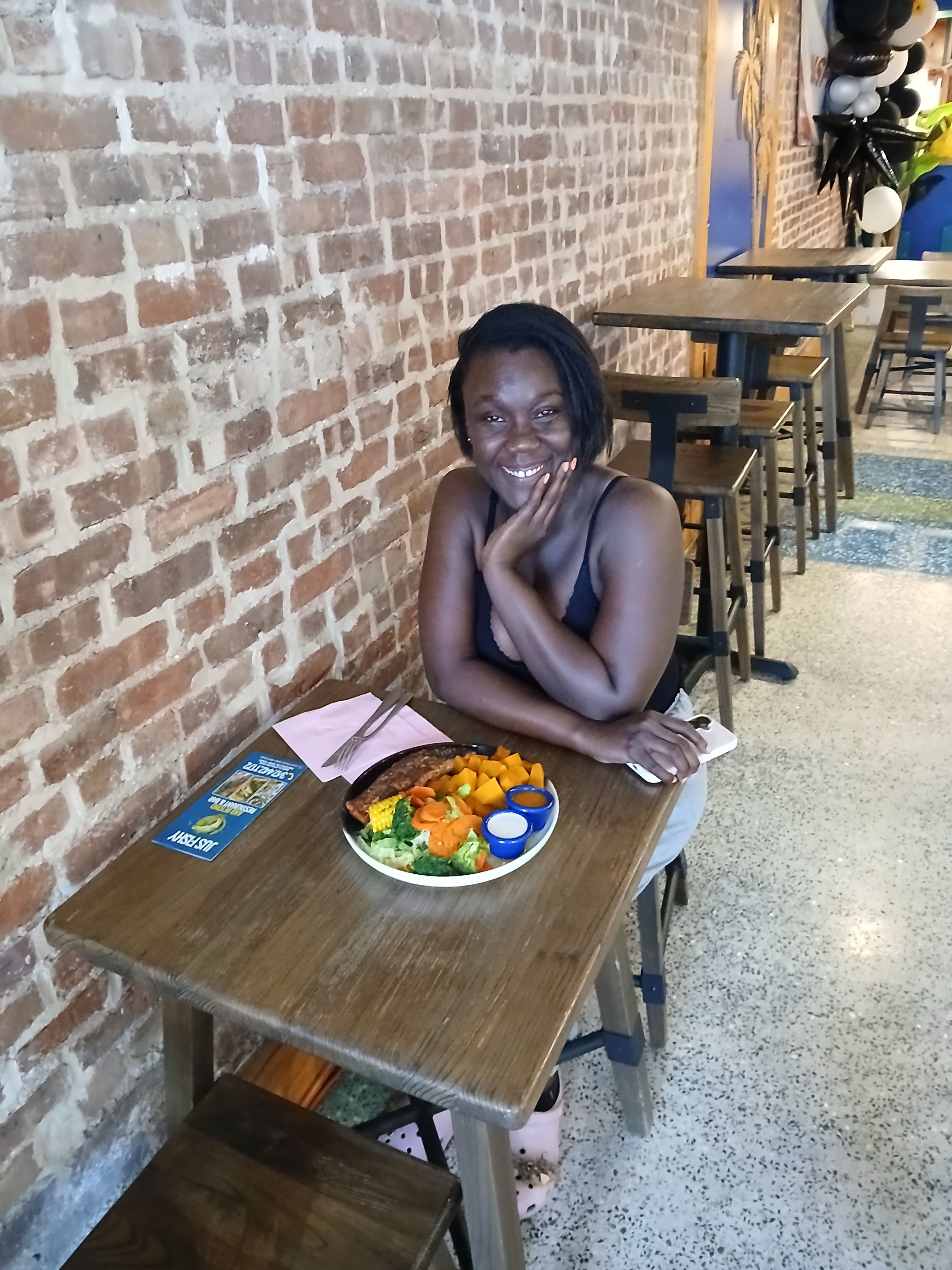A customer smiling and enjoying a healthy grilled seafood platter in the rustic, brick-walled dining room of our Flatbush Avenue Brooklyn ny restaurant.