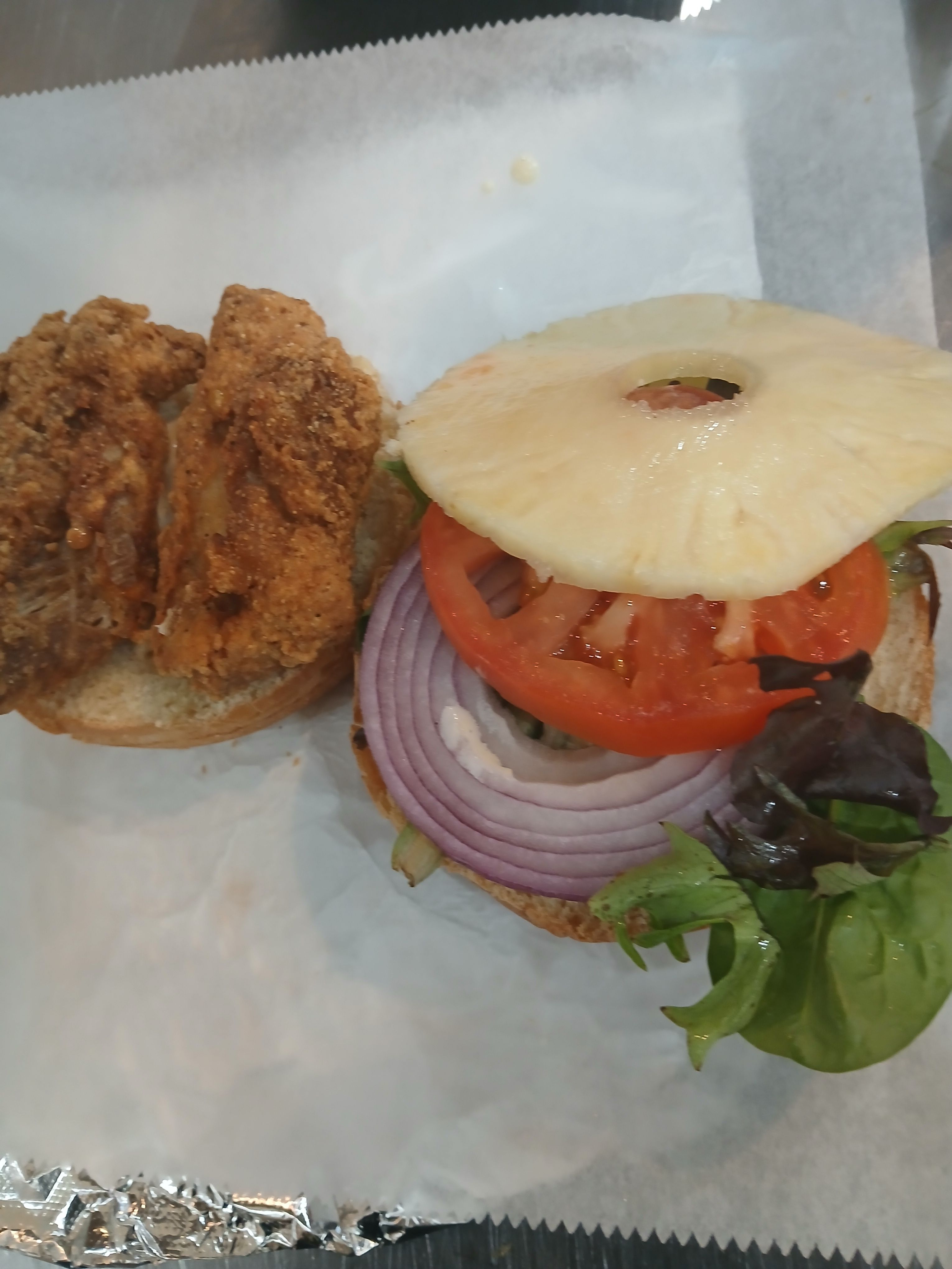  Our signature Caribbean Shark Burger at Jus Fishy & Beyond, featuring crispy seasoned shark fillets topped with a fresh pineapple slice, red onion, tomato, and greens.