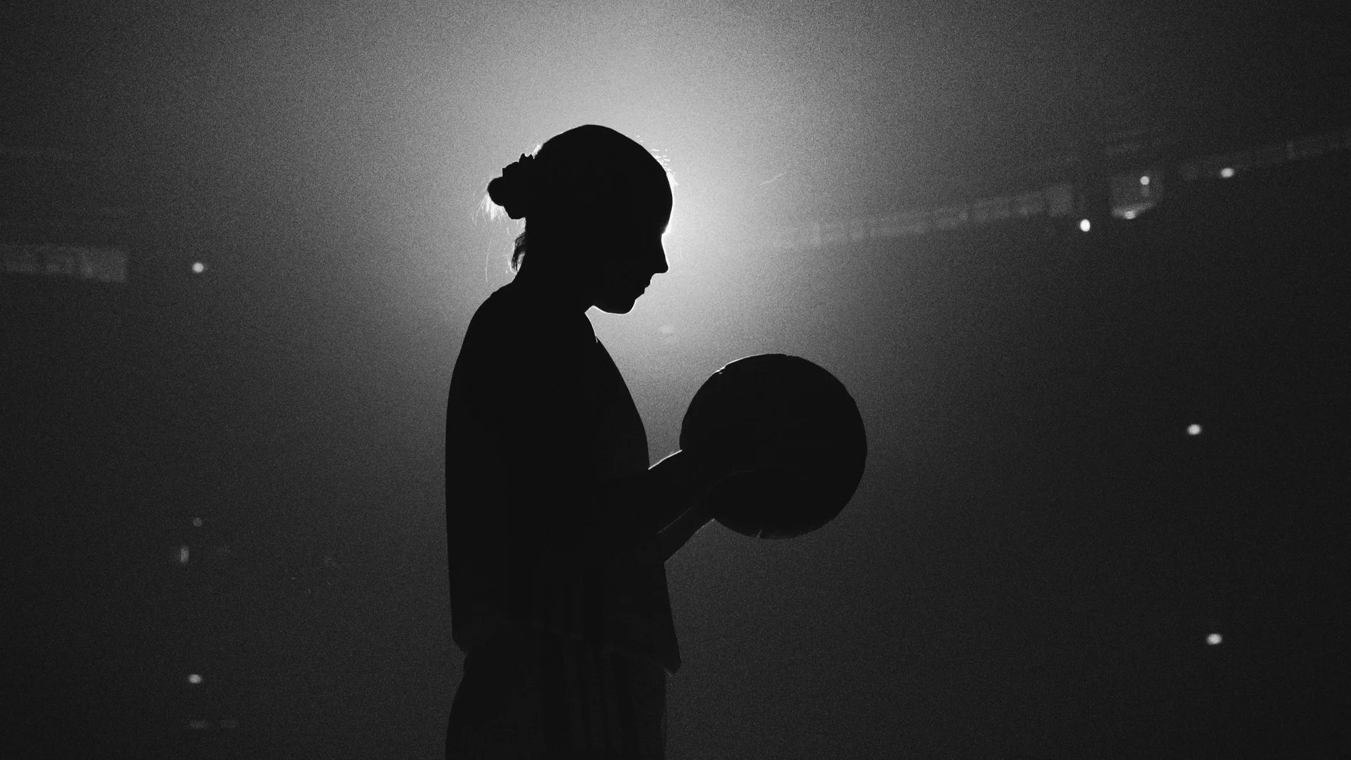Silhouette en noir et blanc d’une joueuse tenant un ballon, devant un halo lumineux.