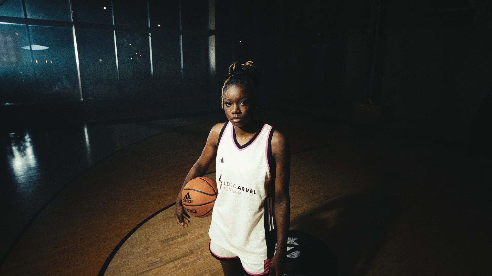 Une joueuse en maillot blanc et rose tient un ballon sur le parquet.