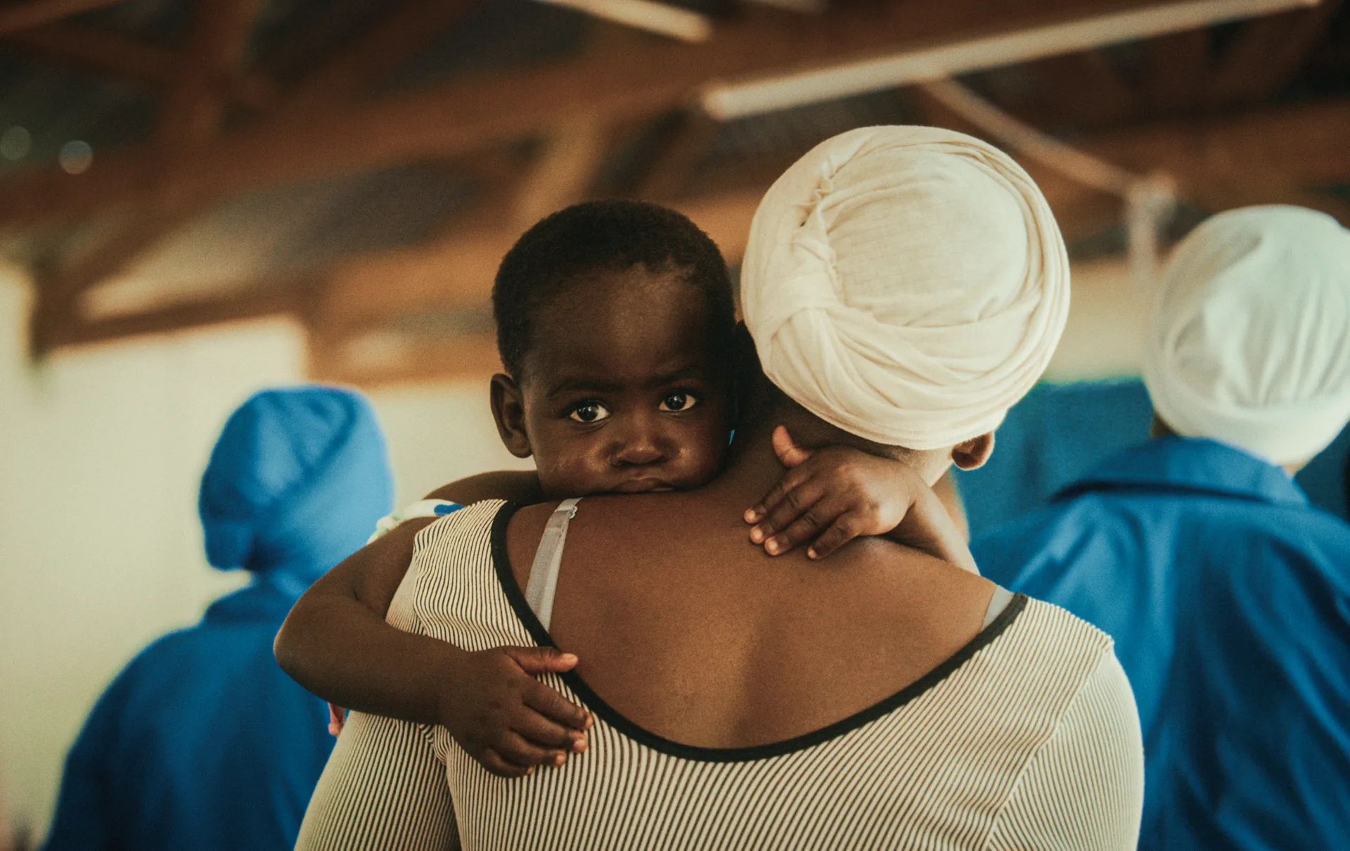 Un enfant regarde l'objectif dans les bras d'une femme.
