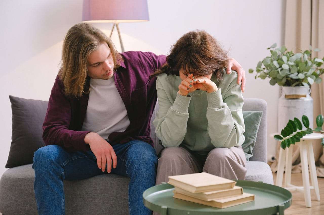 man soothing crying sad woman on sofa