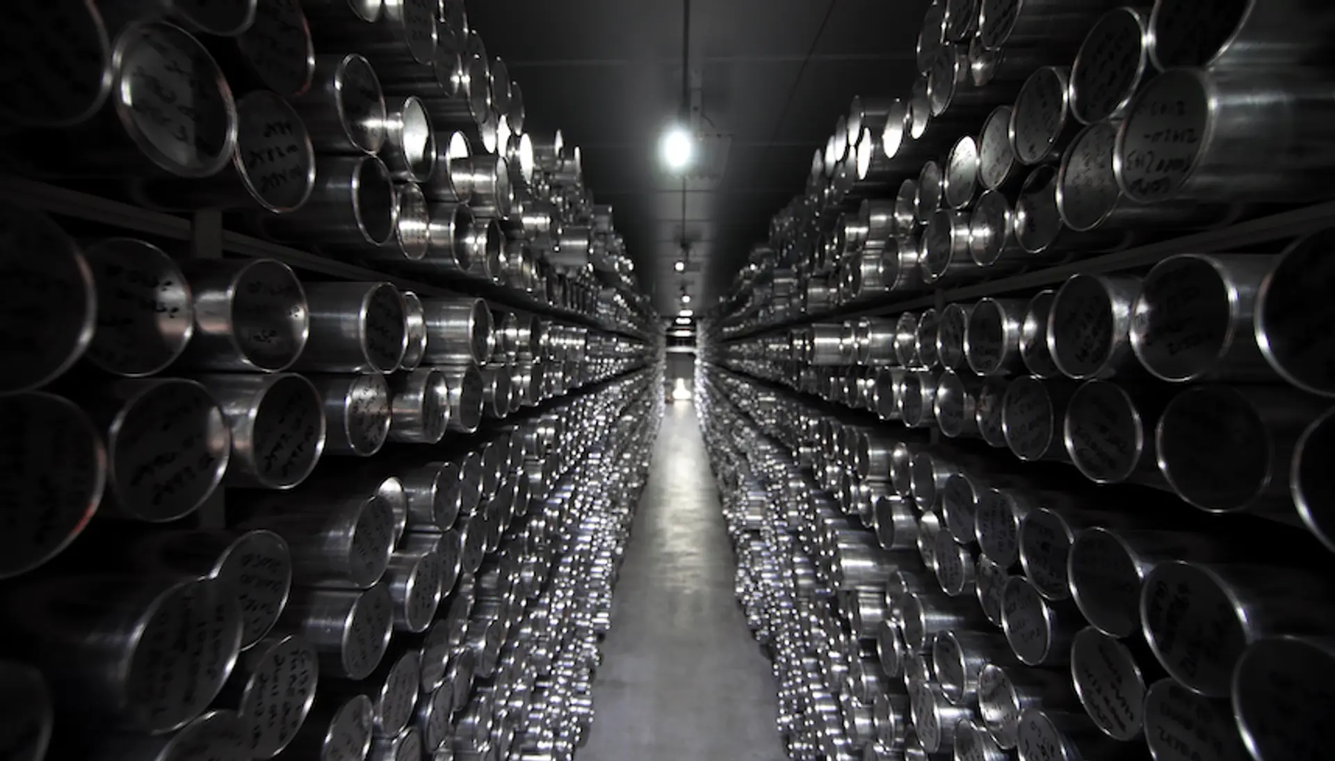 Shelves with silver cylindrical containers recede into the background of a dark indoor space