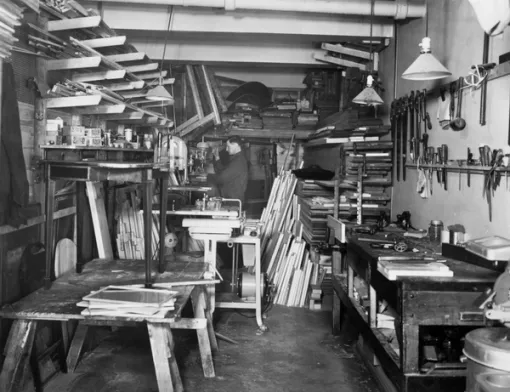 A carpenter shop filled with materials and tools. A man works in the background.