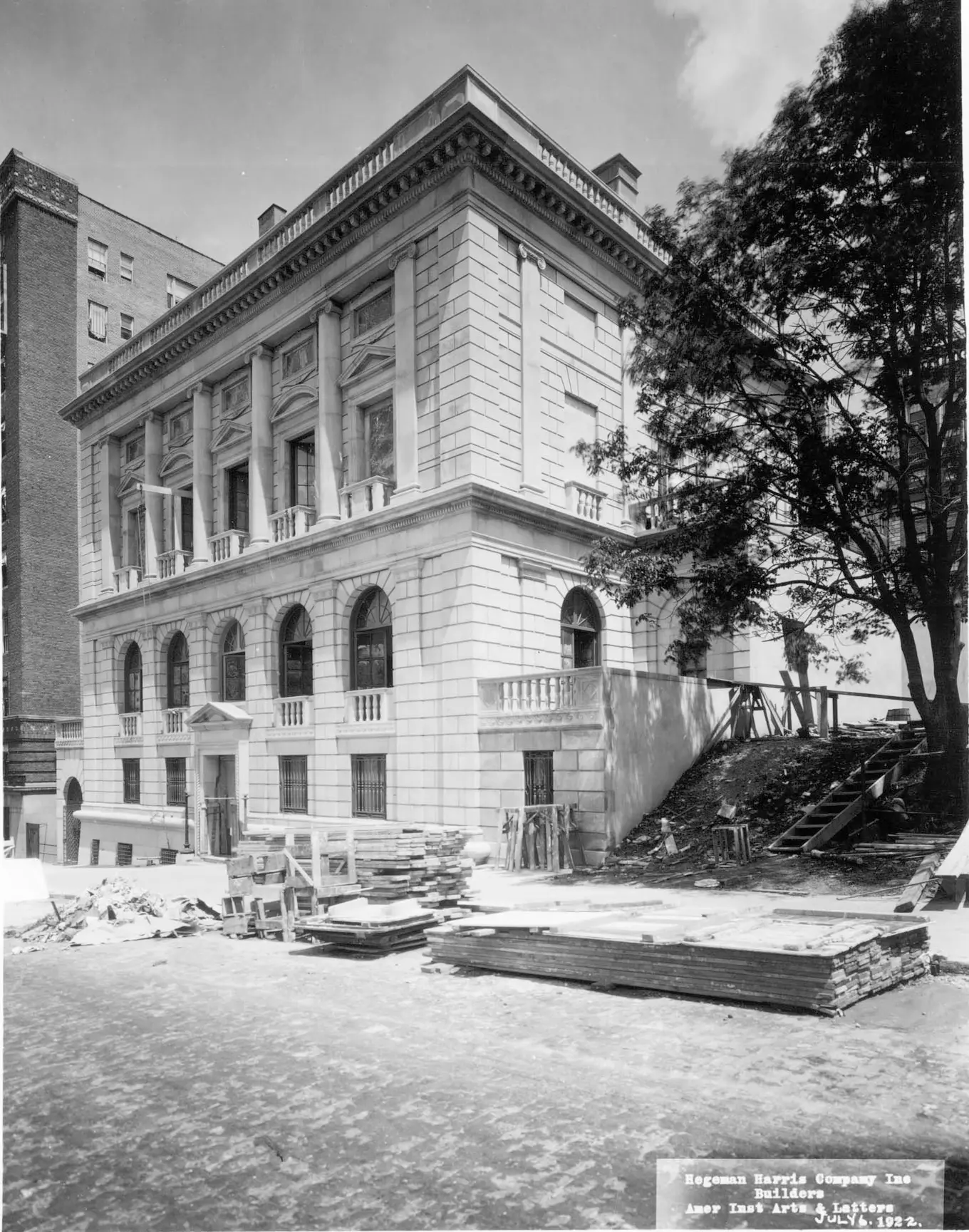 A black and white photograph of the exterior of the American Academy of Arts and Letters. In front of the building, building materials sit in the road.