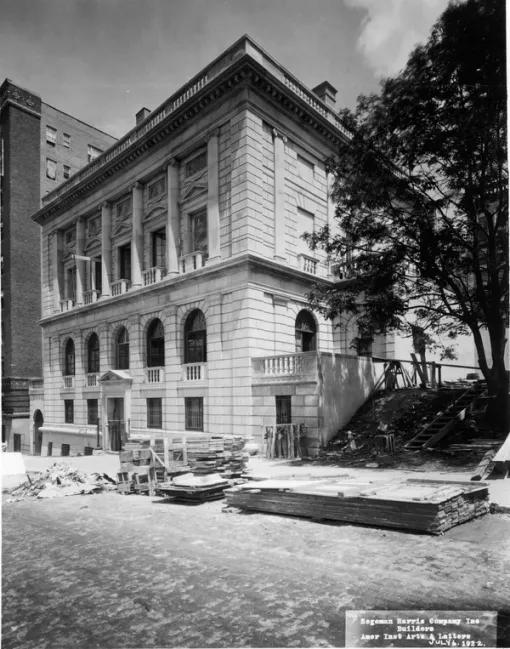 A black and white photograph of the exterior of the American Academy of Arts and Letters. In front of the building, building materials sit in the road.