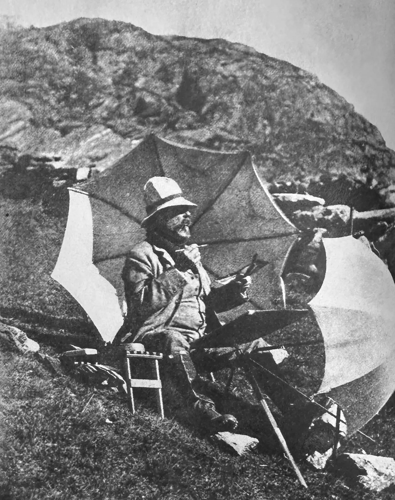 A black and white photograph of a man painting on a hillside.