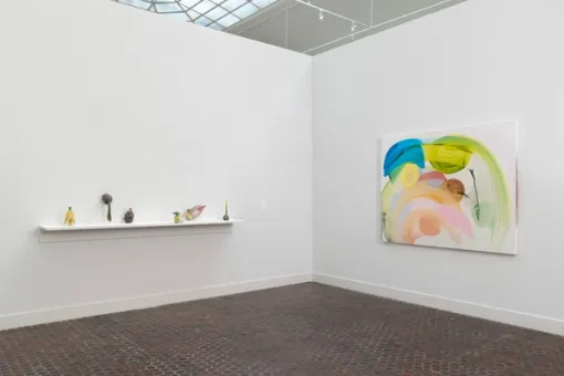 A series of small ceramic sculptures sit on a shelf mounted to a wall. To the right, a large colorful abstract painting hangs on the adjacent wall.