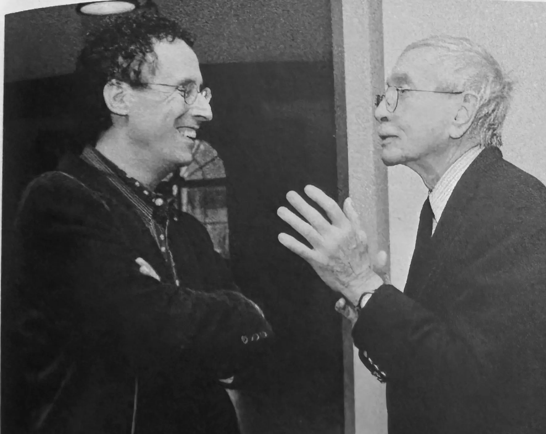 A black and white photograph of two men in conversation. On the left, Tony Kushner laughs as Edward Albee gestures with his hands.