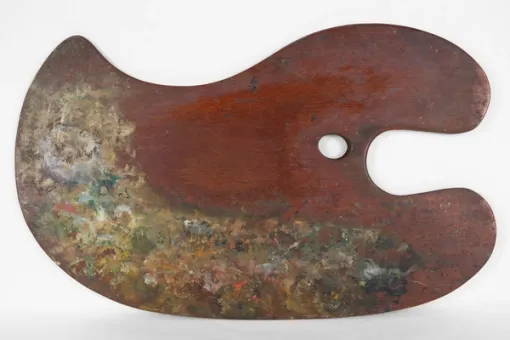 Photograph of a curved, oblong wooden painter’s palette with daubs of paint in various colors