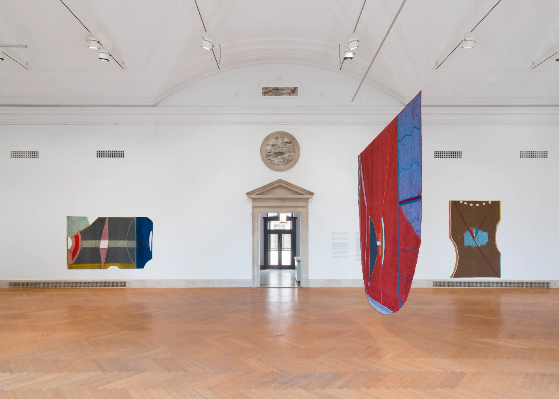 View of three large paitnings in a gallery space; two are on the wall, one is suspended in space