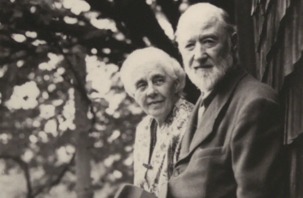 A black-and-white photograph shows a middle-aged man and woman looking at the camera amidst a backdrop of nature.