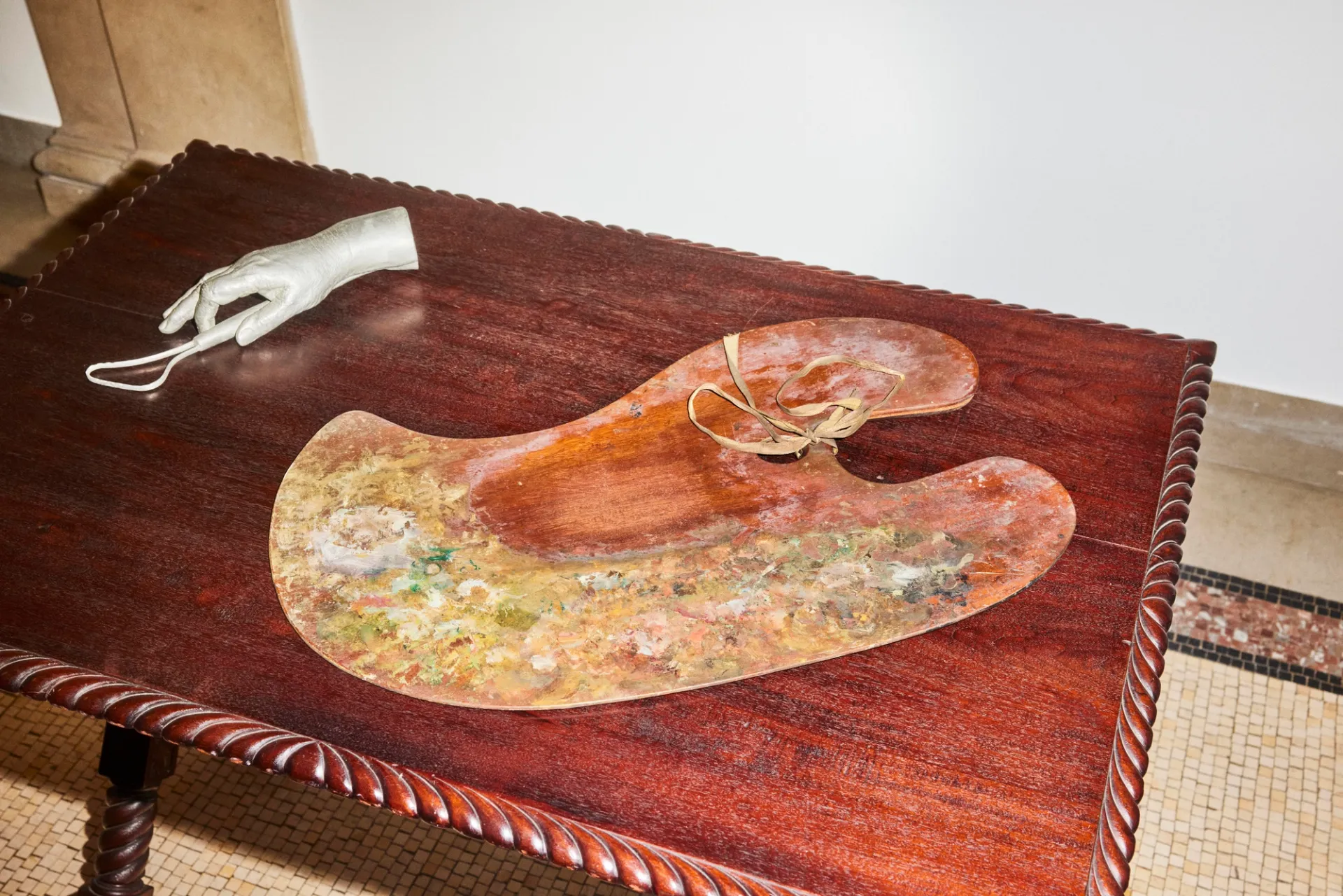 A cast of a hand and a painters' palette rest on a wooden table