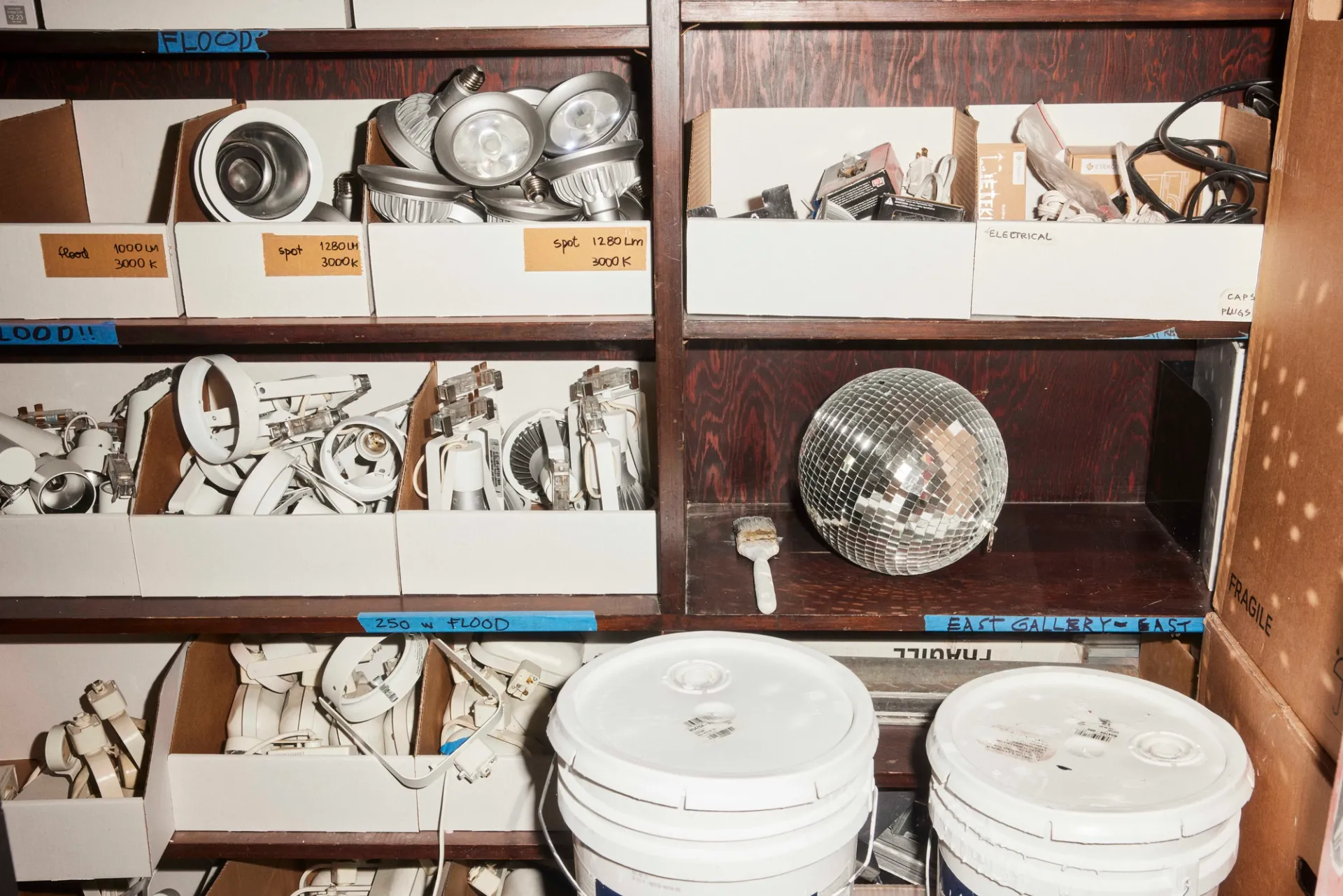 Photograph of a supply closet with gallery bulbs, paint buckets, and a small disco ball.