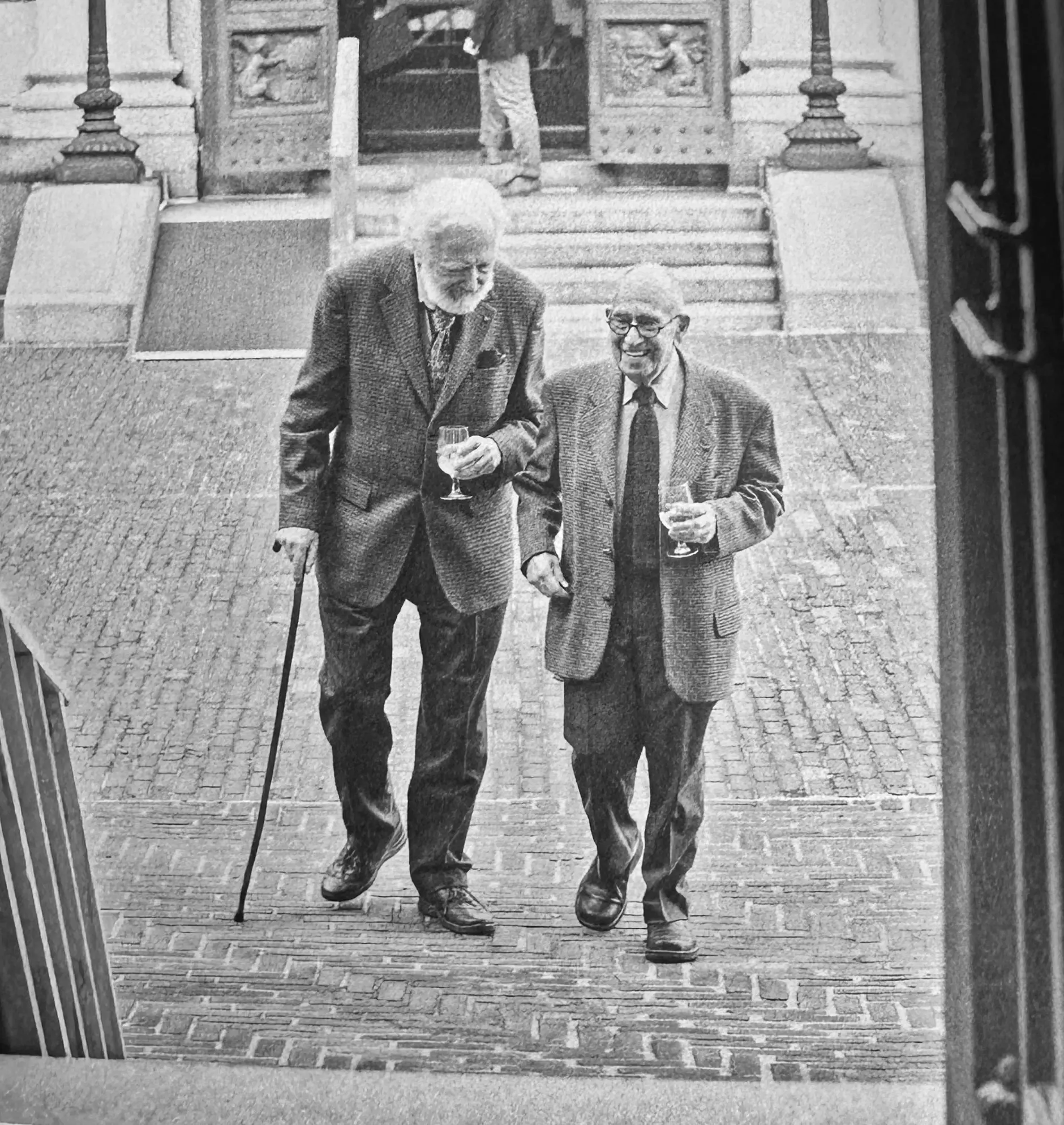 A black and white photograph of two older men smiling as they walk beside each other in Audubon Terrace.