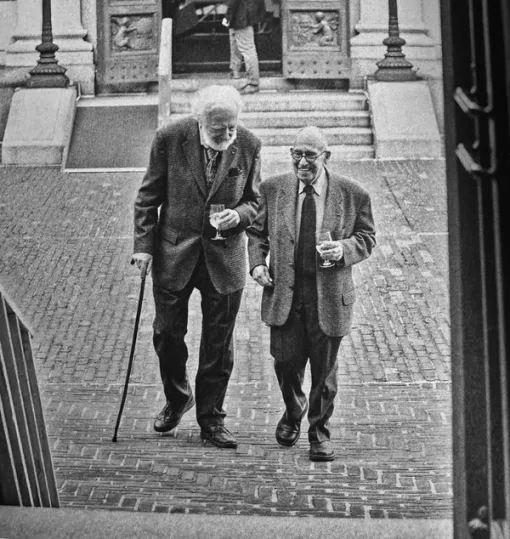 A black and white photograph of two older men smiling as they walk beside each other in Audubon Terrace.