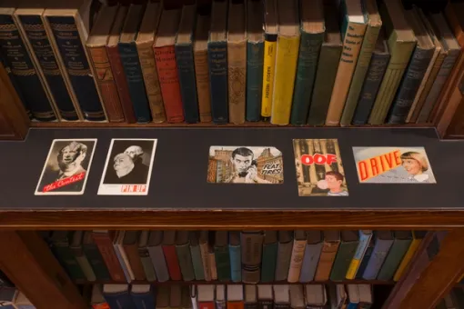 Postcard-sized collages along a bookshelf ledge
