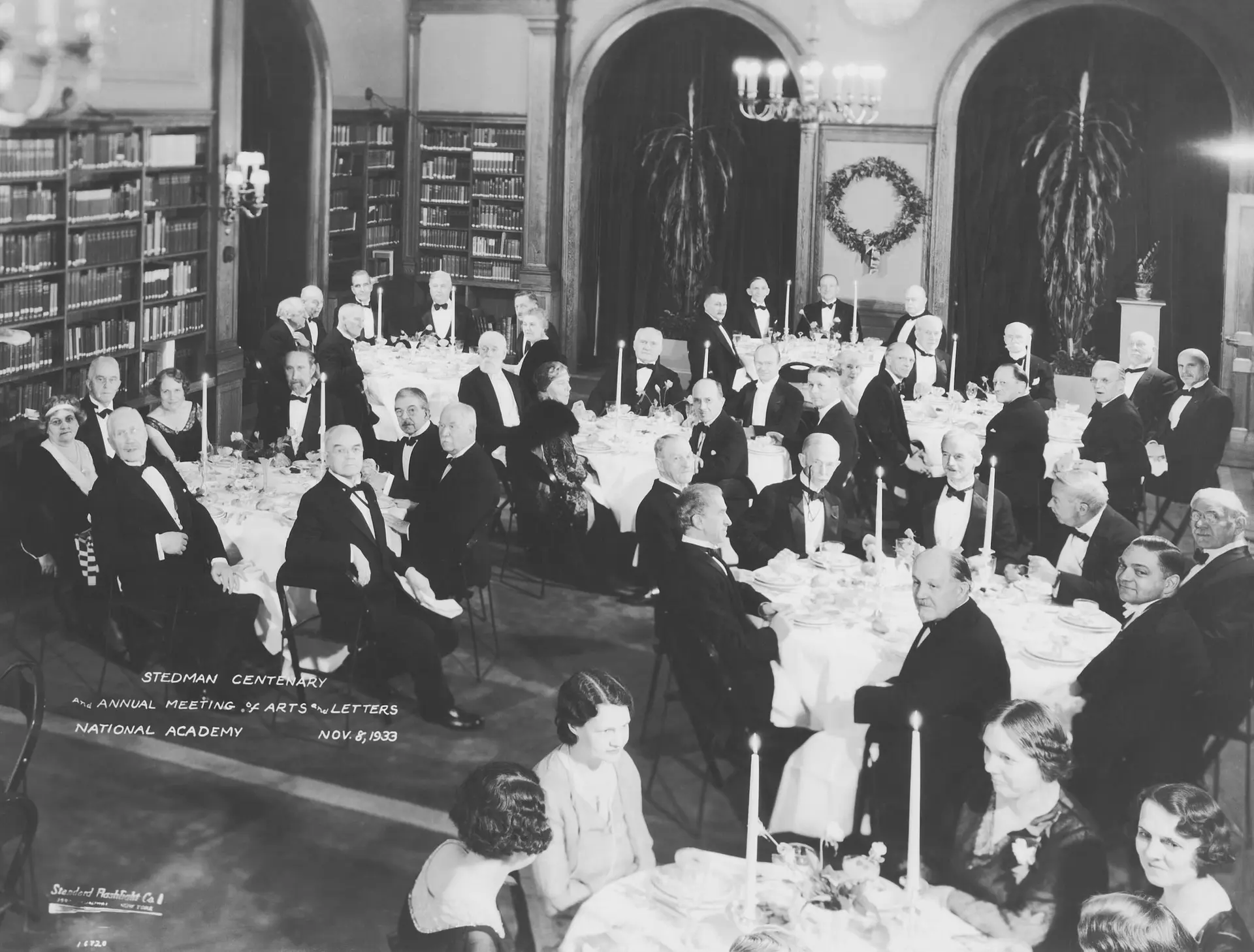 A library filled with several dozen people seated at round dining tables