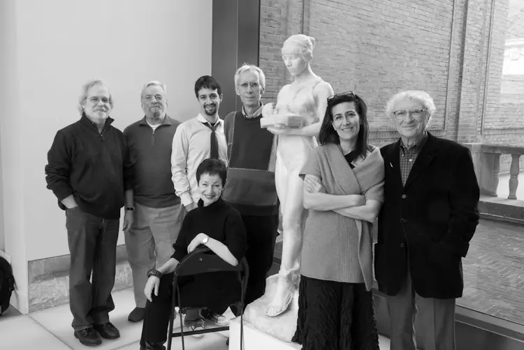 A black and white photograph of seven people posing beside a marble statue of a woman.