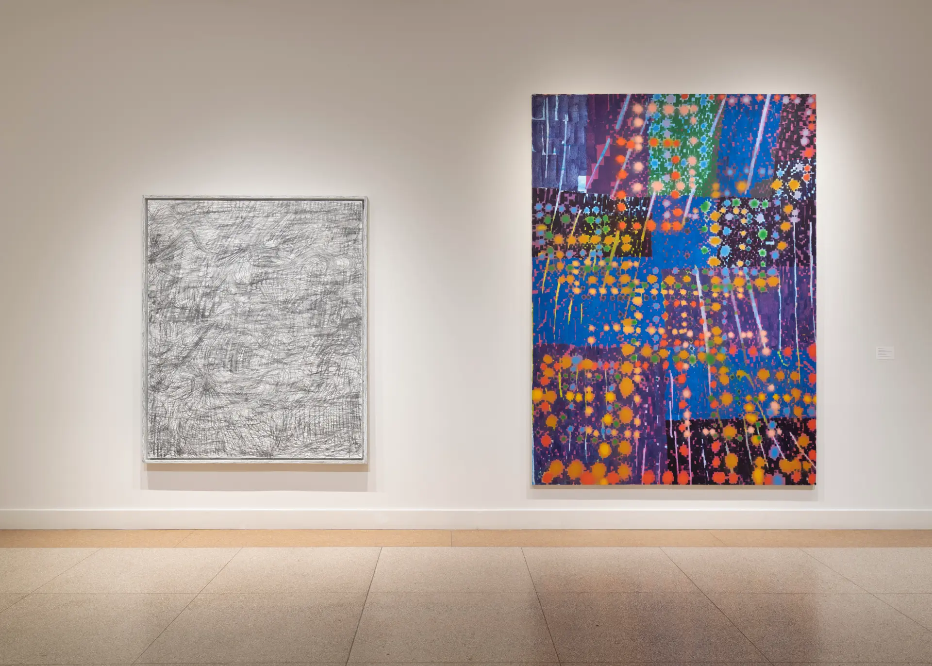 Two large paintings, one gray and the other an assortment of colors, hang mounted on a wall.