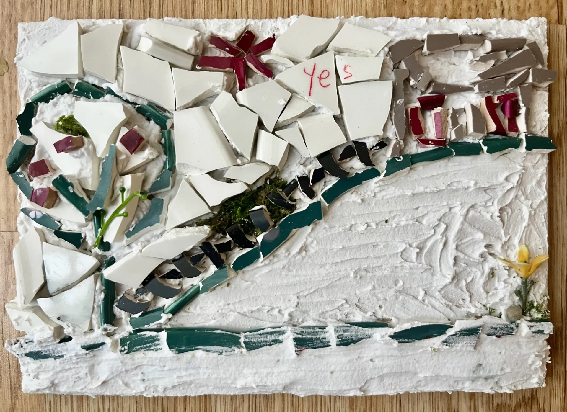 white mosaic against wooden board. The word "yes" is handwritten in red across fragments.
