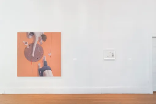 On a wall, a large painting showing two shirtless boys crawling on a peach background hangs beside a small framed work on paper.