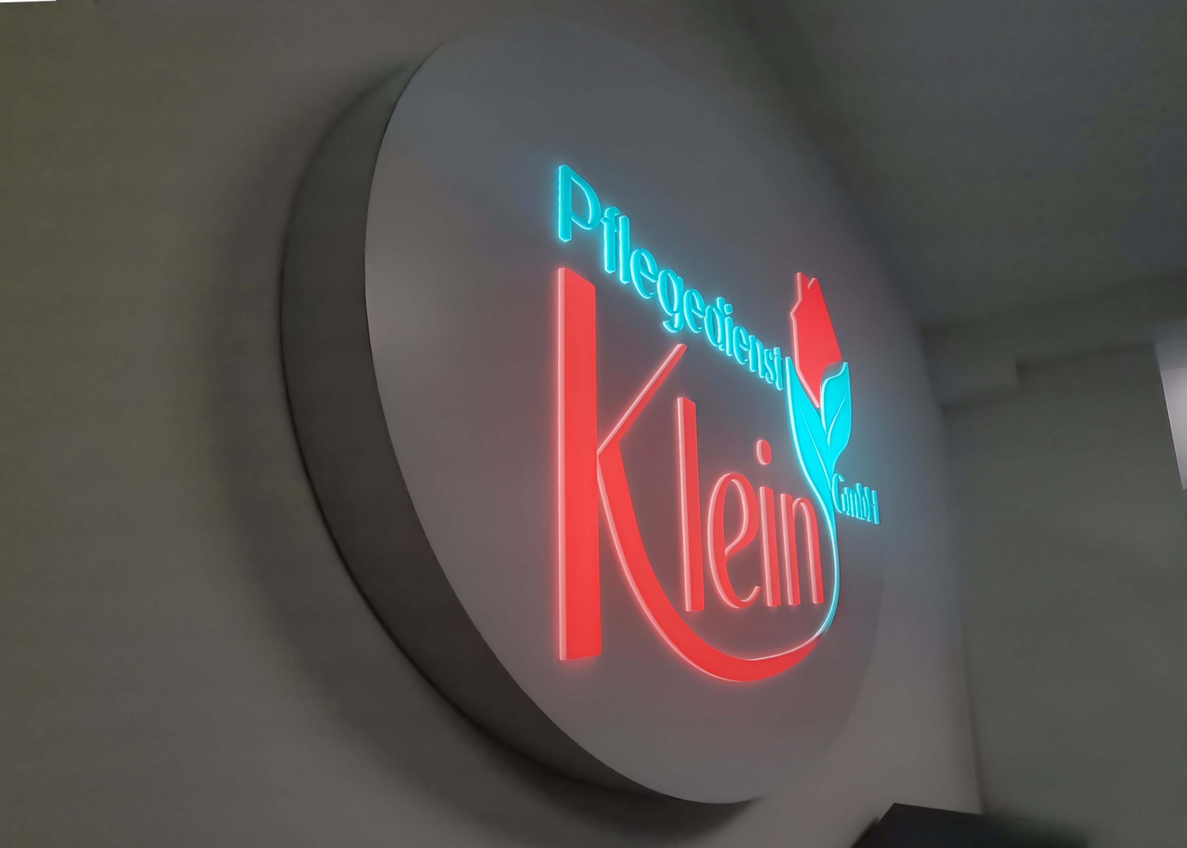 Runder Leuchtkasten mit leuchtender Schrift und Logo an einer Wand