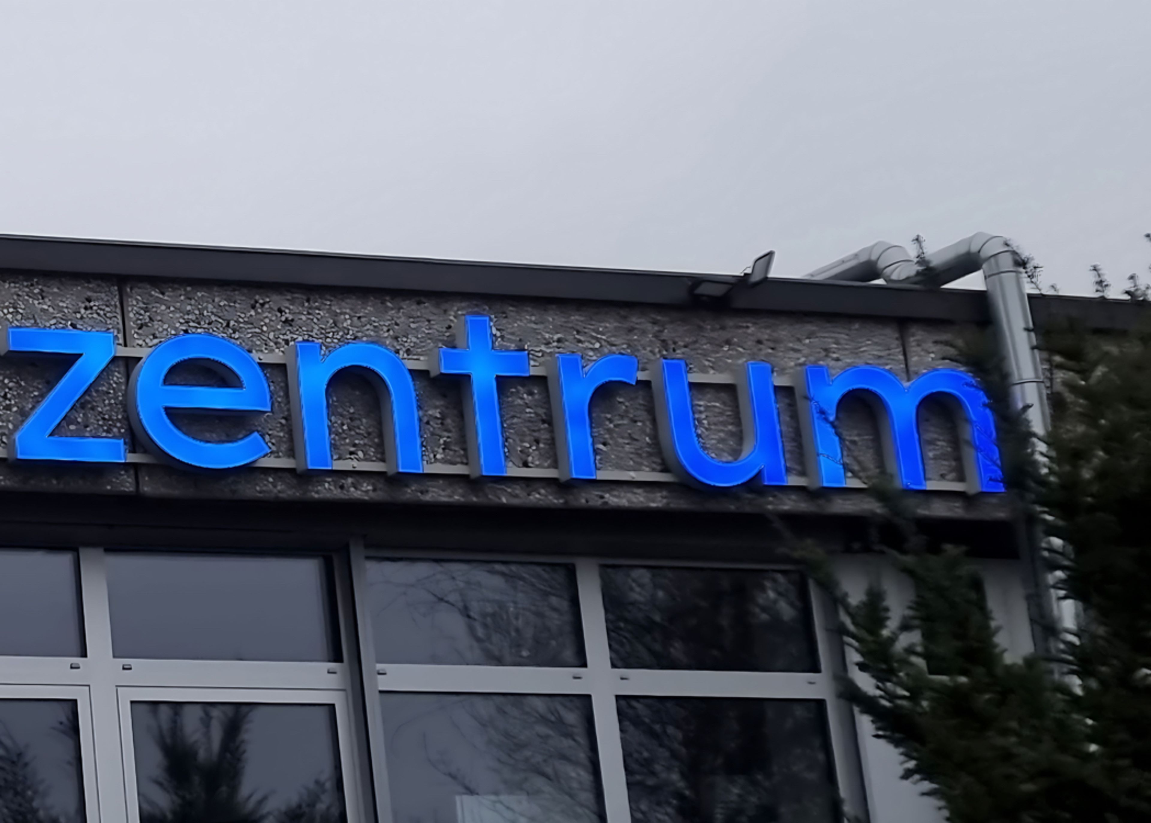 Nahaufnahme der blauen Leuchtbuchstaben „zentrum“ am Tierärztezentrum, darunter die Fensterfront