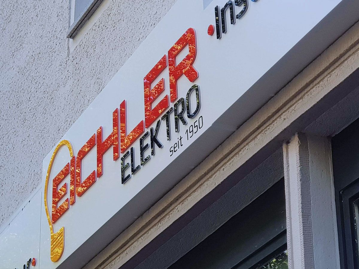 Nahaufnahme eines weißen Leuchtkastens mit erhabener Schrift in Rot und Schwarz und einer Glühbirne als Logo