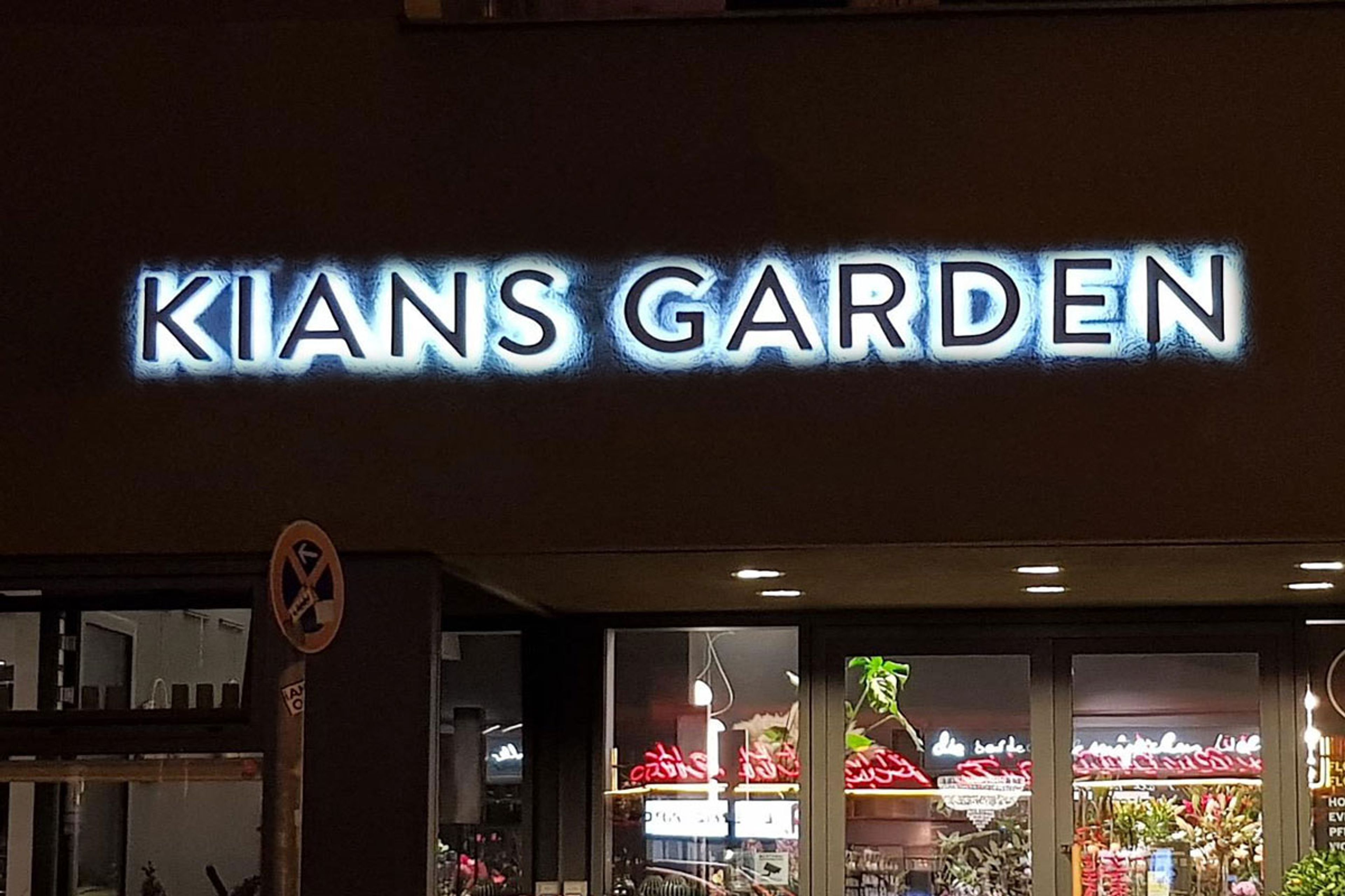 Dunkle Buchstaben mit hellem Lichtkranz an einer dunklen Fassade über einem Laden am Abend