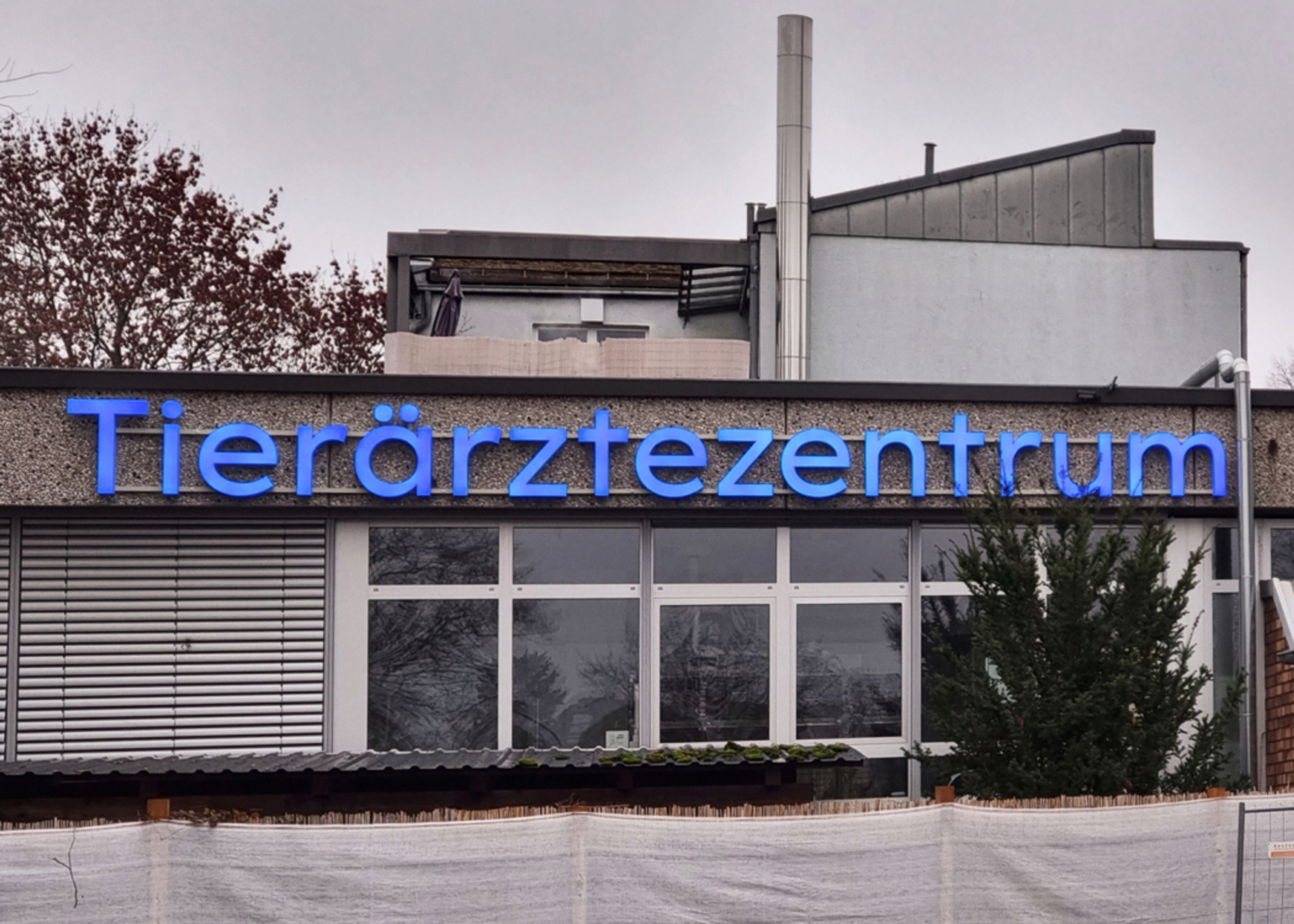 Blaue Leuchtbuchstaben „Tierärztezentrum“ über der Fensterfront eines flachen Gebäudes, bei Tag