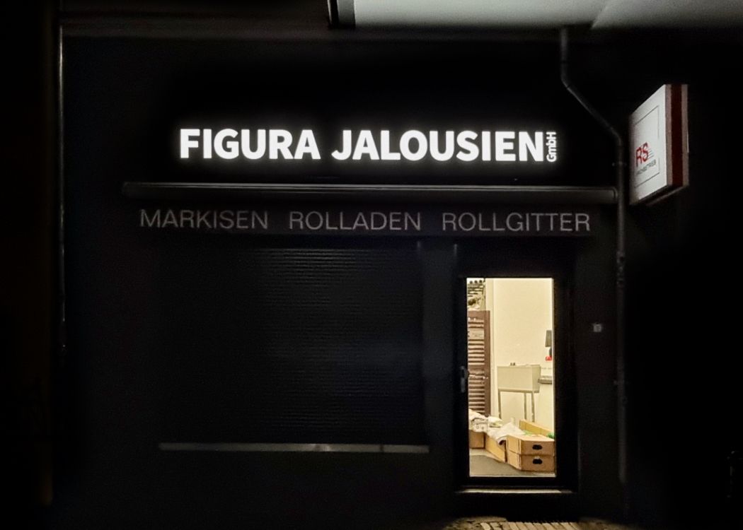 Leuchtende Schrift auf dunkler Blende über einem Schaufenster am Abend