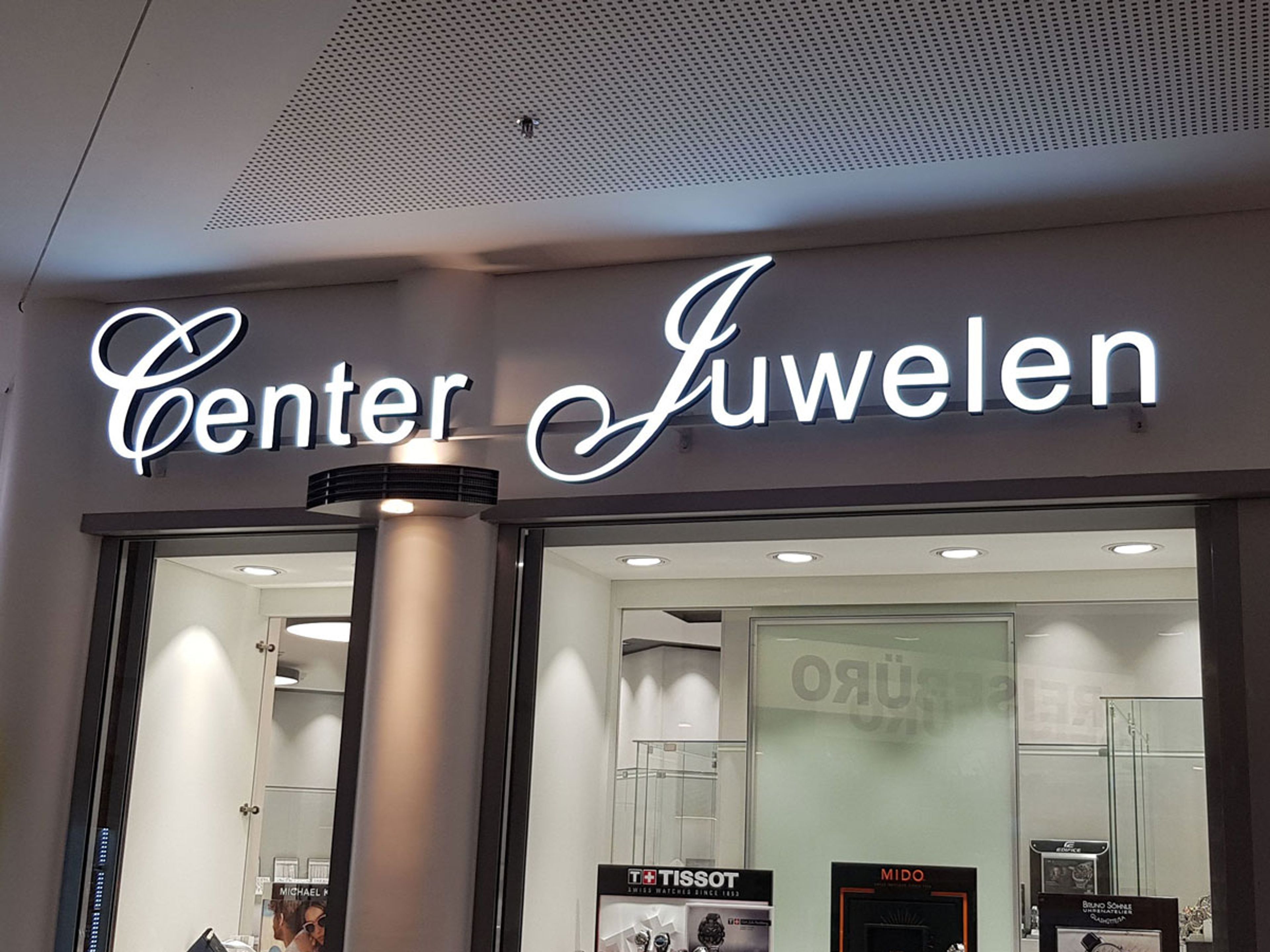 Leuchtender Schriftzug „Center Juwelen“ frontal über den Schaufenstern eines Juweliergeschäfts im Innenbereich