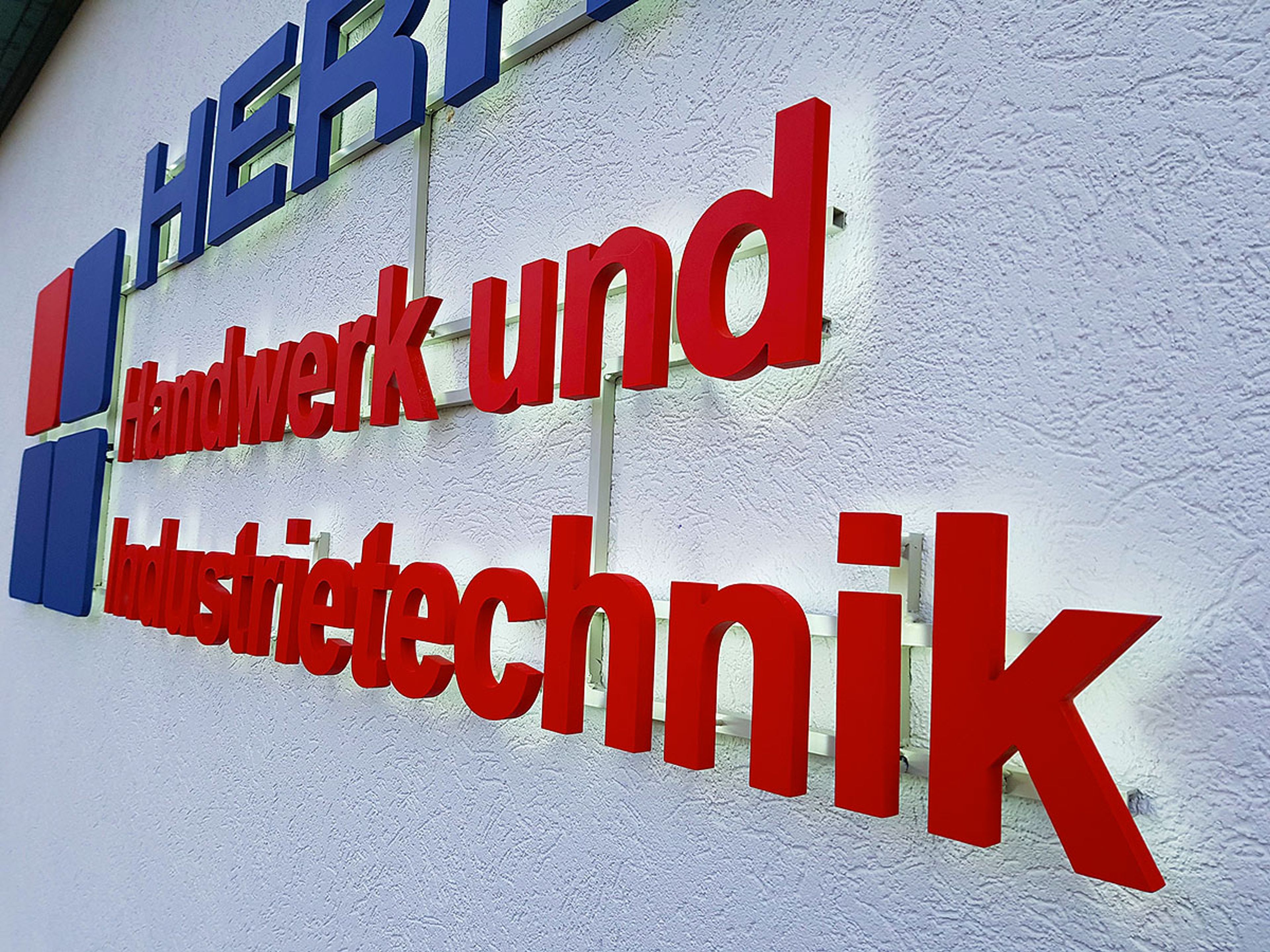 Nahaufnahme roter Buchstaben auf Abstandshaltern mit Montageschienen an einer weißen Putzwand, schräg von der Seite