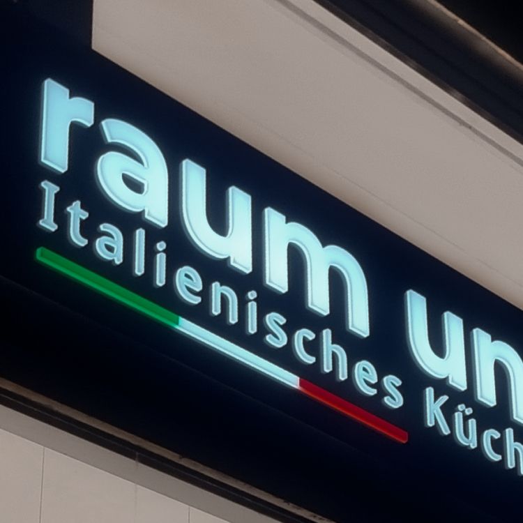 Nahaufnahme der leuchtenden, erhabenen Schrift „Raum und Küche“ mit Streifen in Grün, Weiß und Rot auf dunklem Grund