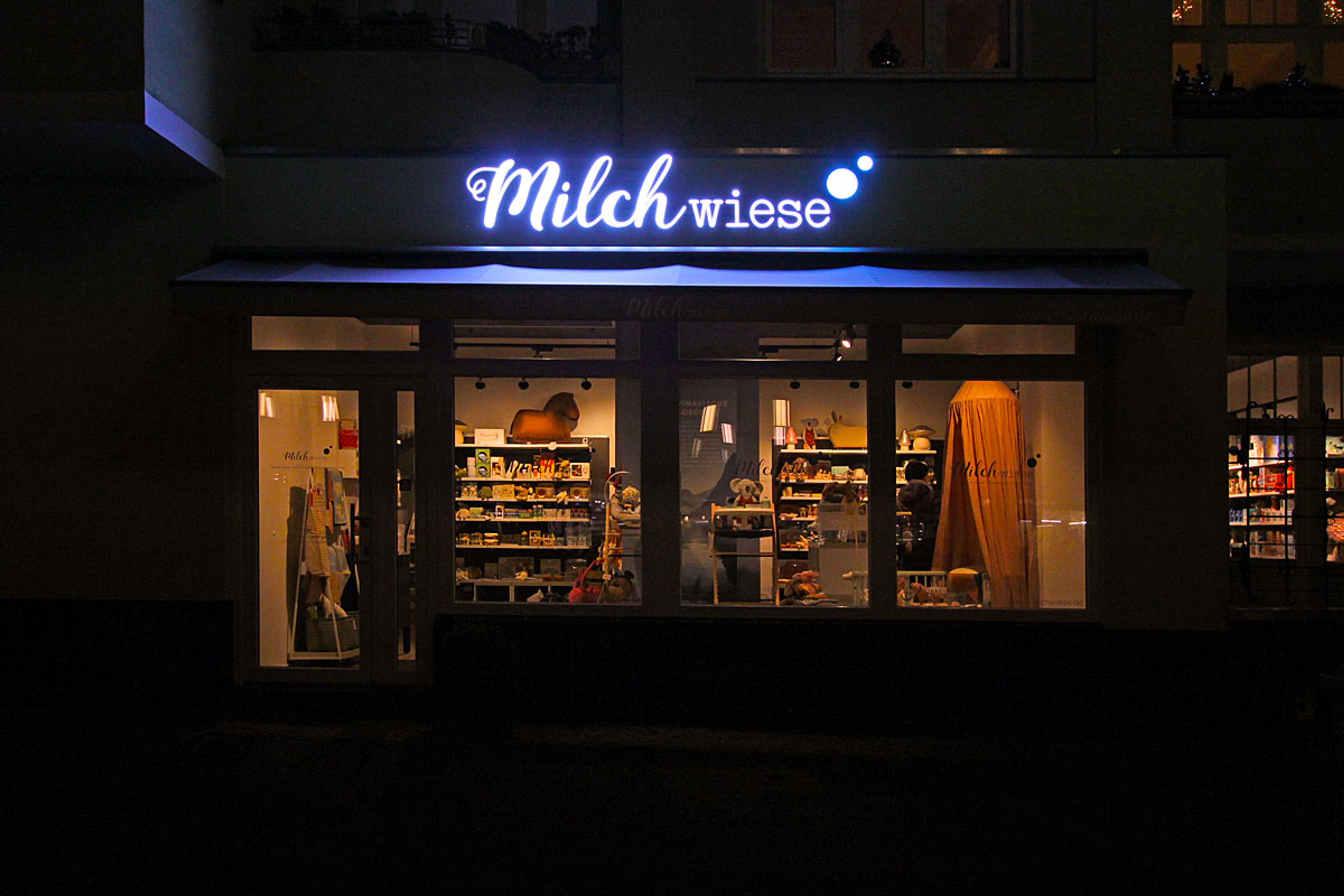 Leuchtbuchstaben in Schreibschrift über einem Ladenfenster am Abend