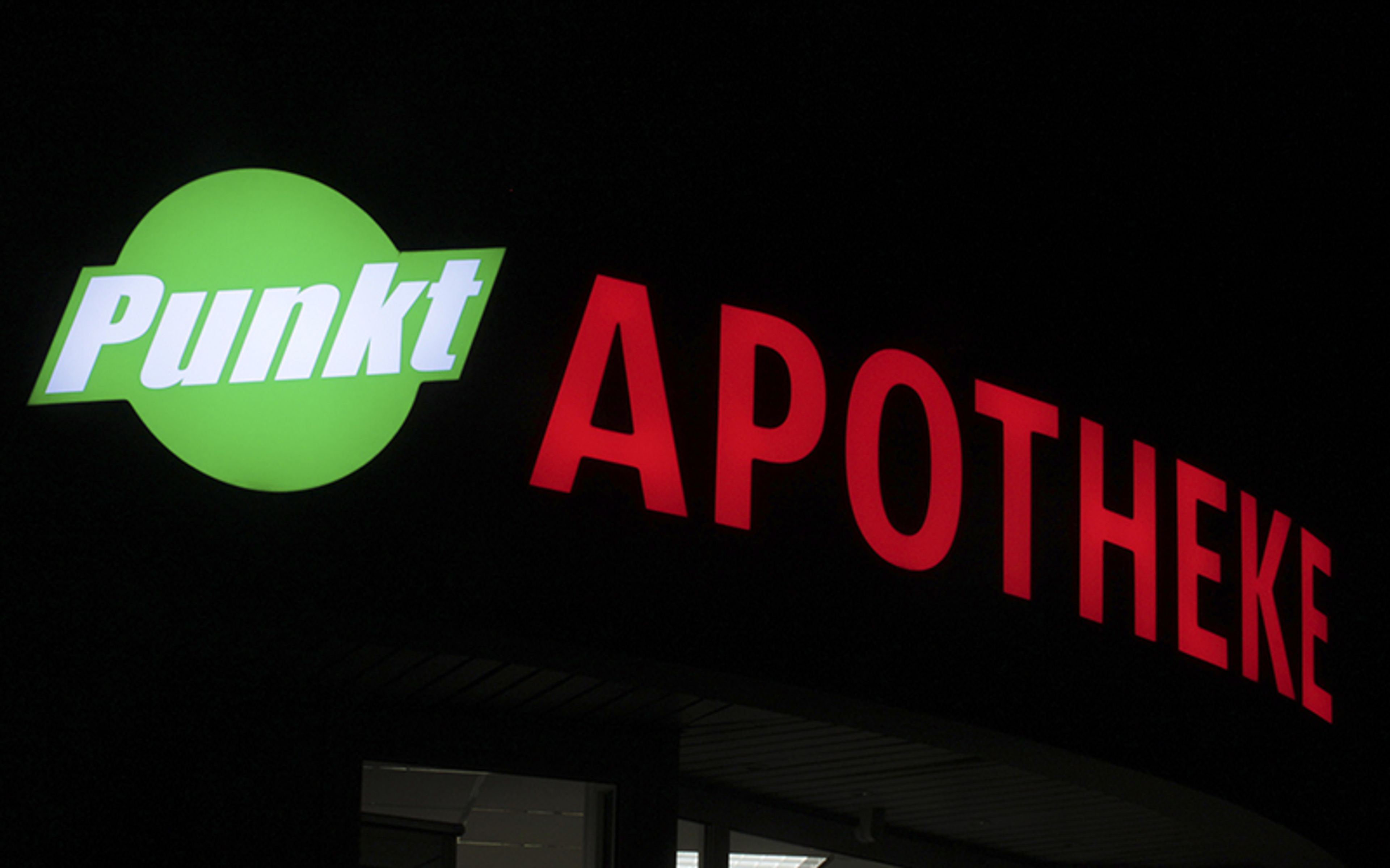 Leuchtschrift und rundes Logo einer Apotheke an der Fassade bei Nacht