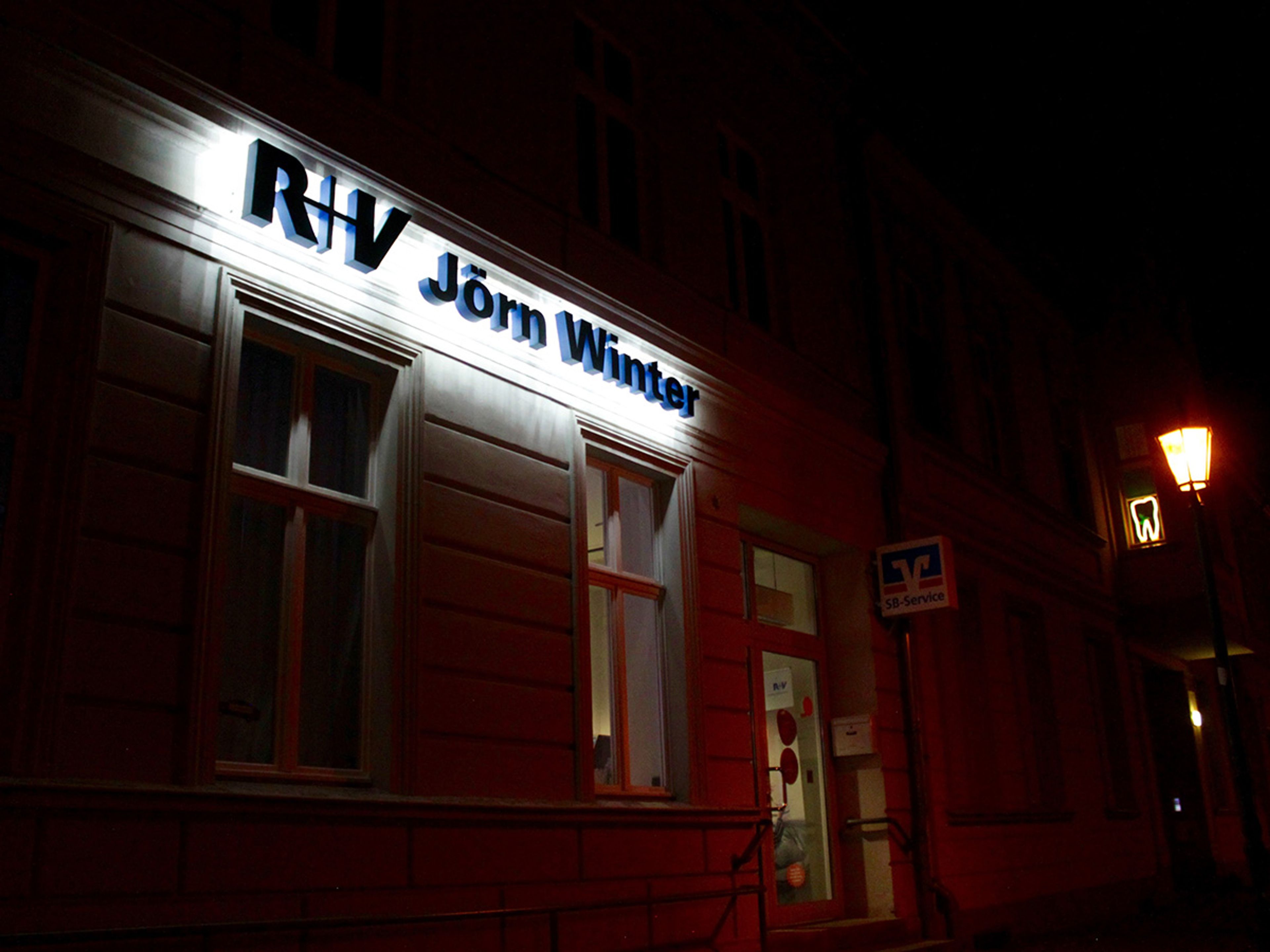 Leuchtbuchstaben mit Logo an einer Hausfassade am Abend