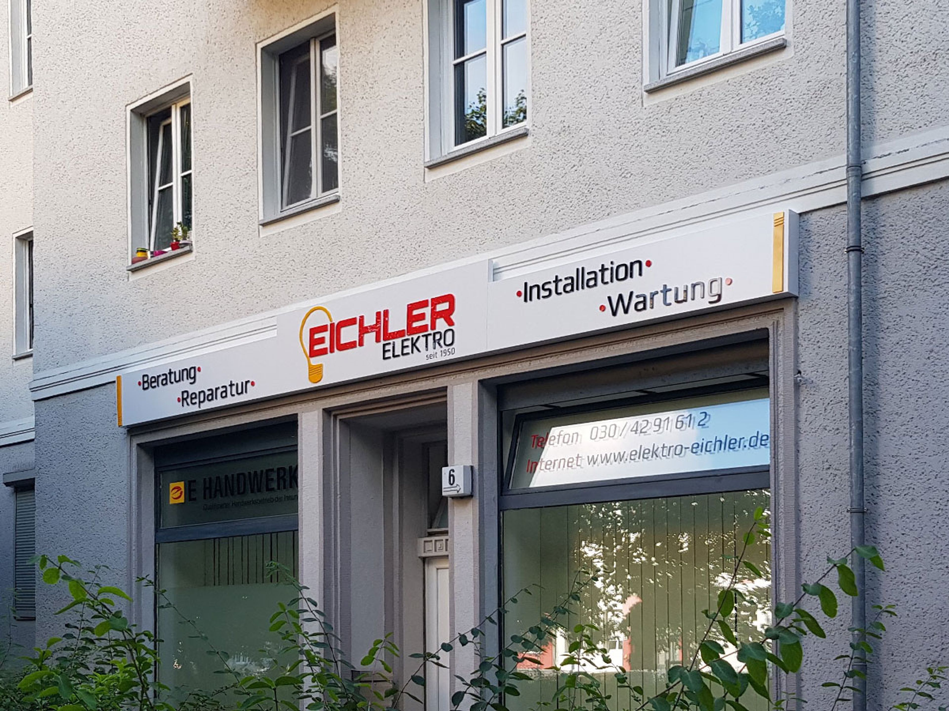Weißer Leuchtkasten über einem Ladengeschäft im Erdgeschoss eines Wohnhauses, bei Tag