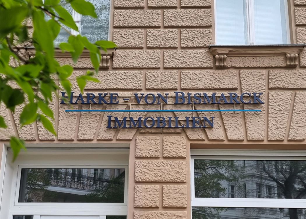Schriftzug eines Immobilienbüros aus dunkelblauen Buchstaben mit blauer Linie über den Fenstern einer Altbaufassade