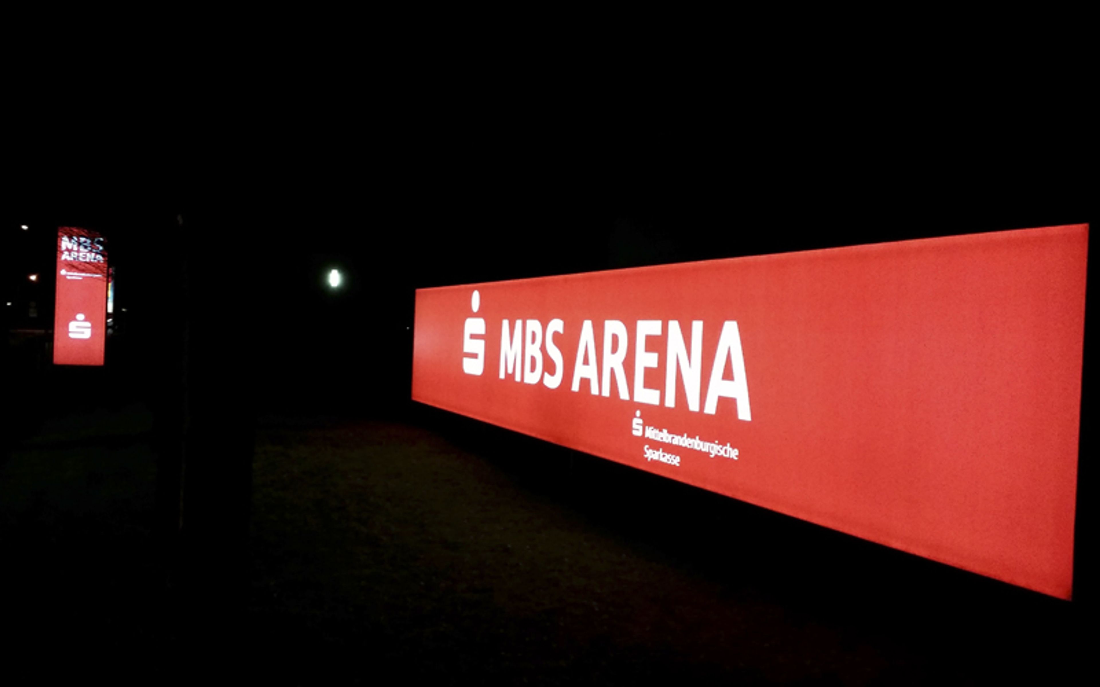 Langer roter Leuchtkasten mit weißer Schrift an einer Halle bei Nacht