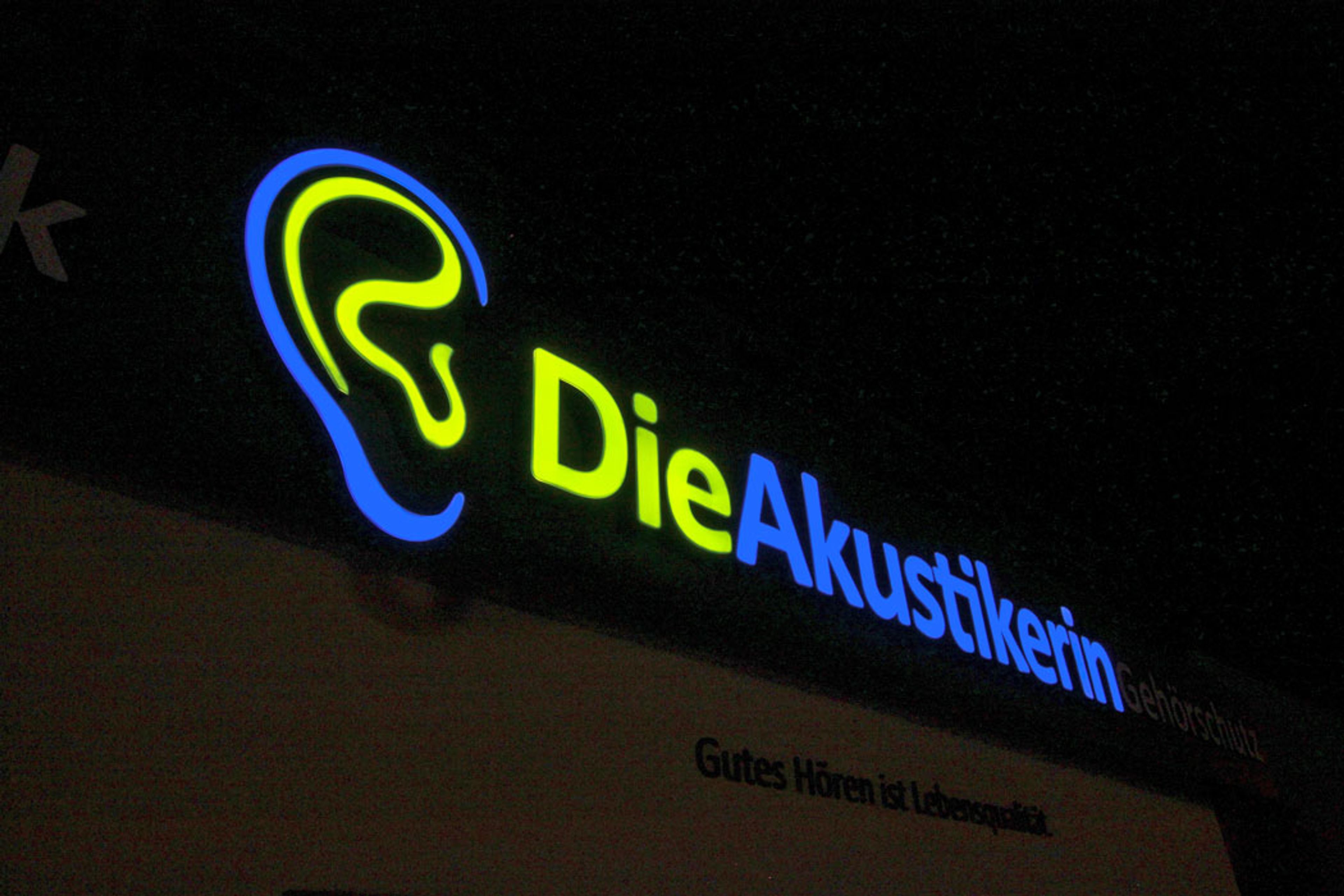 Leuchtbuchstaben mit Logo in Ohrform an einer dunklen Fassade am Abend